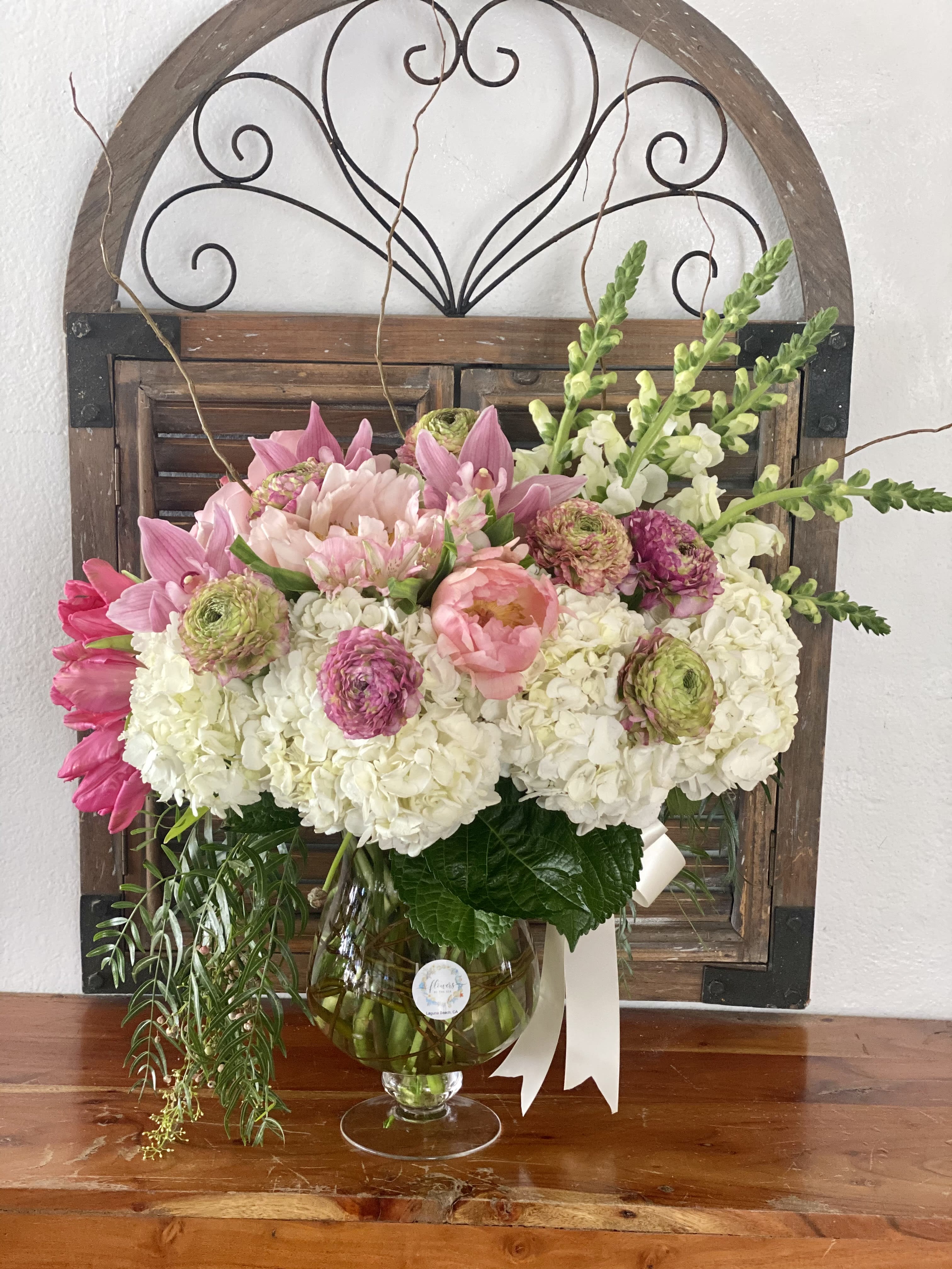 Pink and white floral arrangement in a glass vase with a ribbon