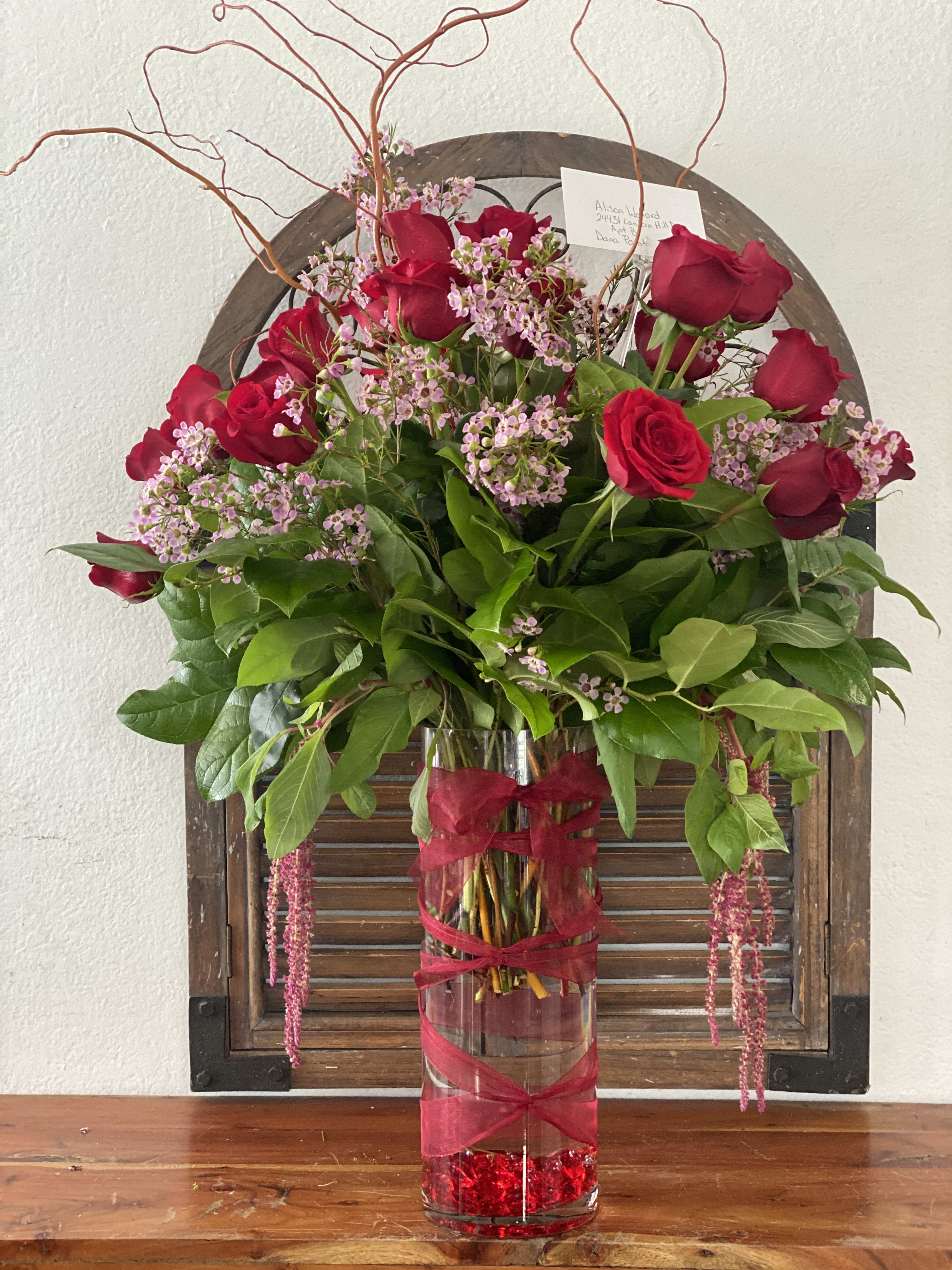 Red roses and pink filler flowers in a tall glass vase with ribbon