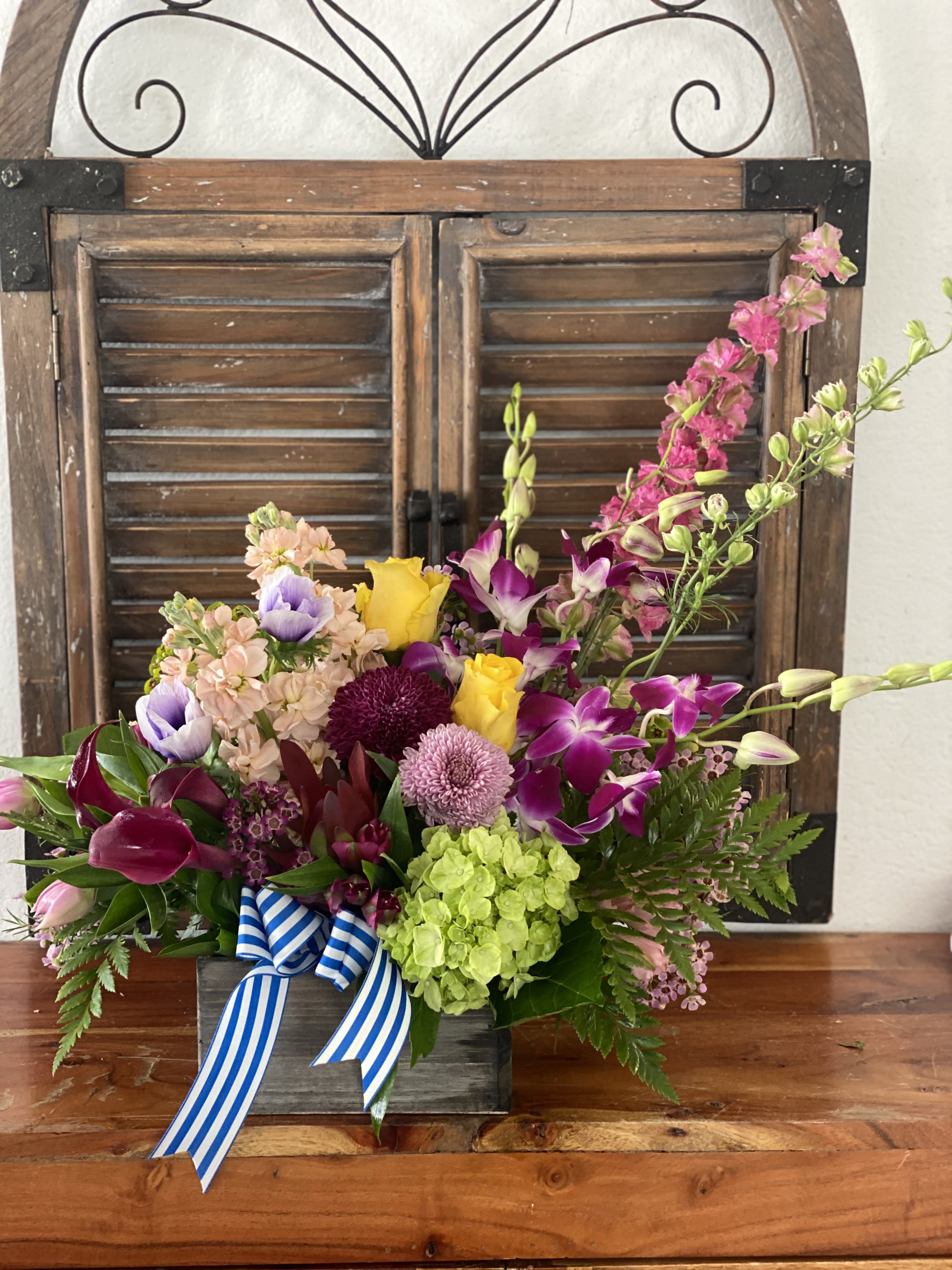 Colorful mixed flower arrangement in a wooden box with a striped ribbon