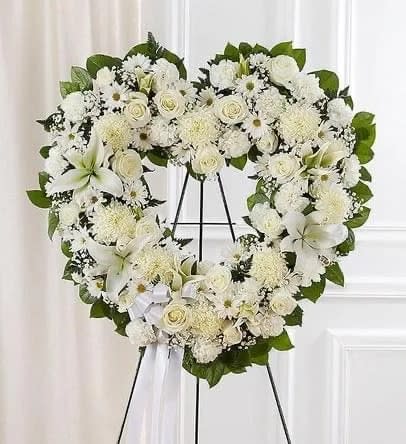 White floral heart wreath on a black stand with a ribbon