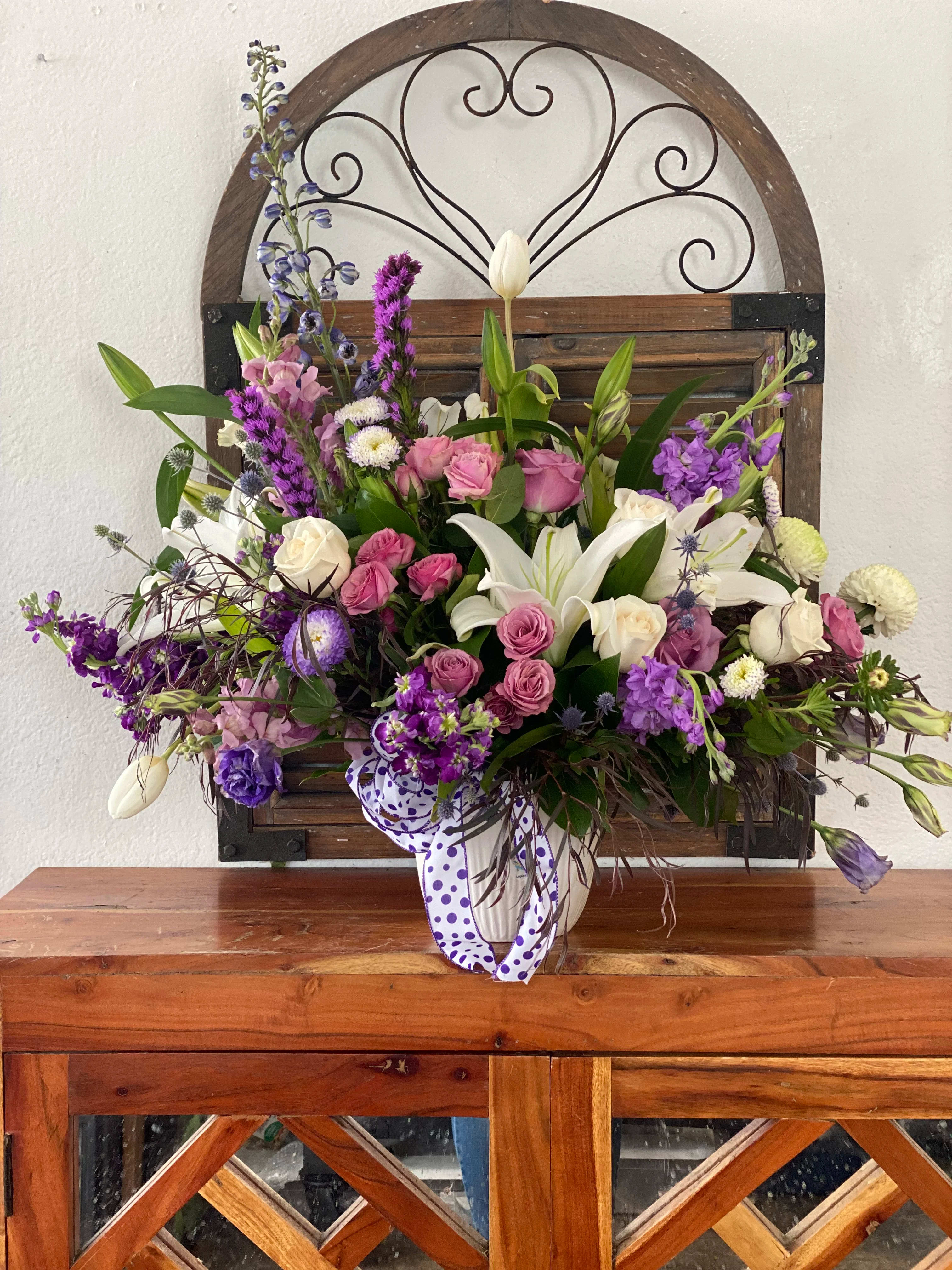 Mixed bouquet with white lilies, pink roses, and purple flowers in a ribbon-tied vase