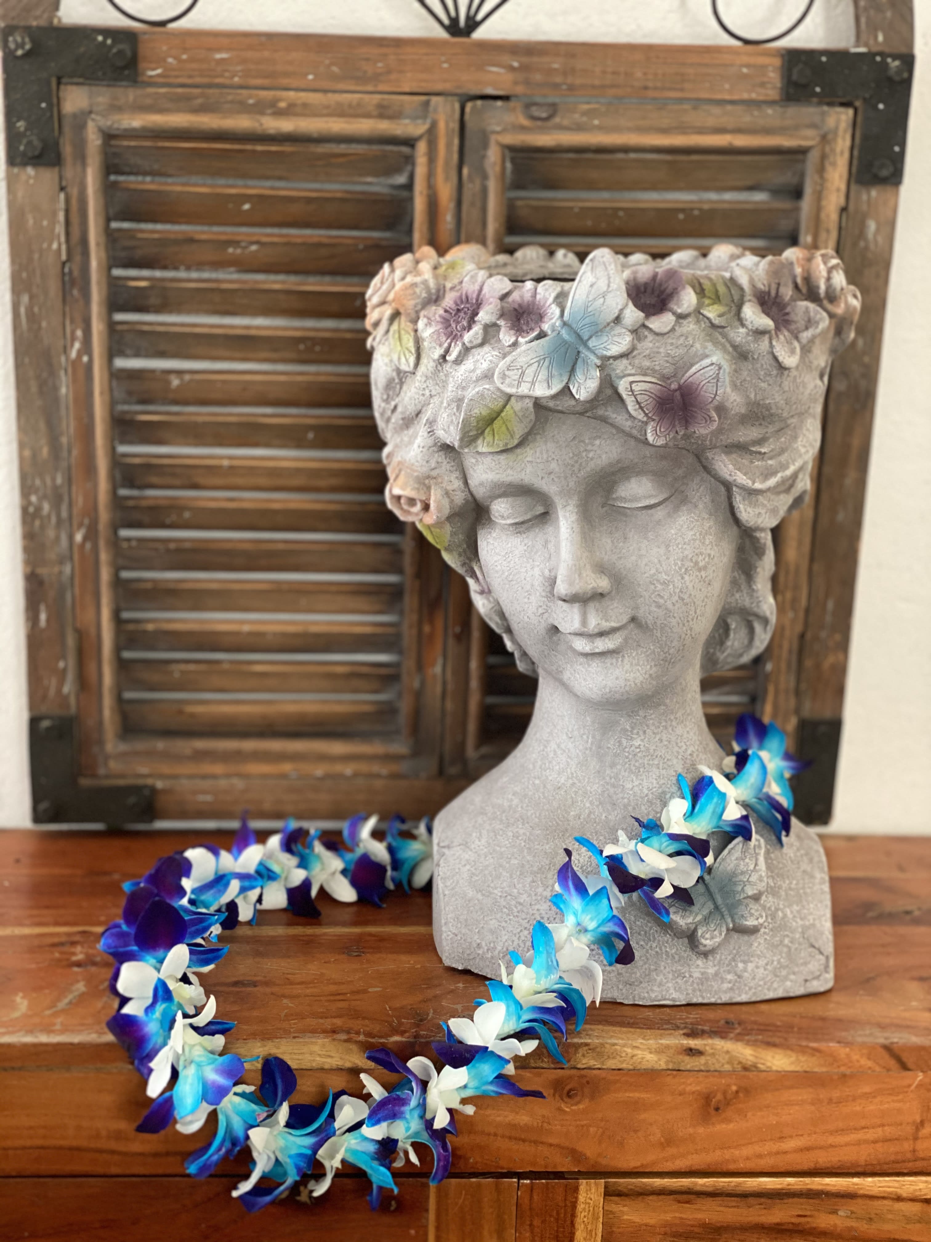 Stone bust planter with butterfly decorations and a blue-white flower lei