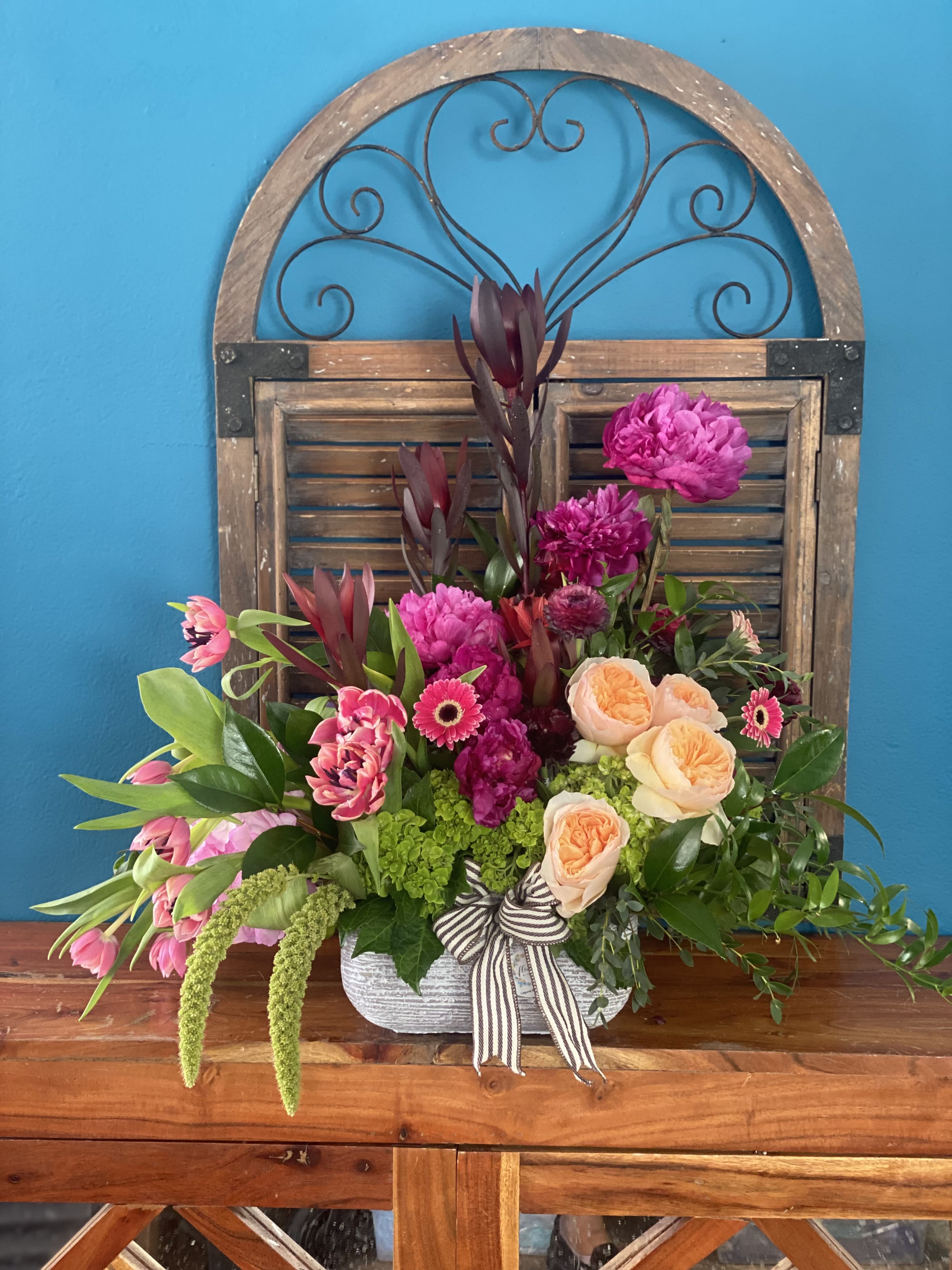 Mixed pink and peach floral arrangement in a white container with a striped ribbon