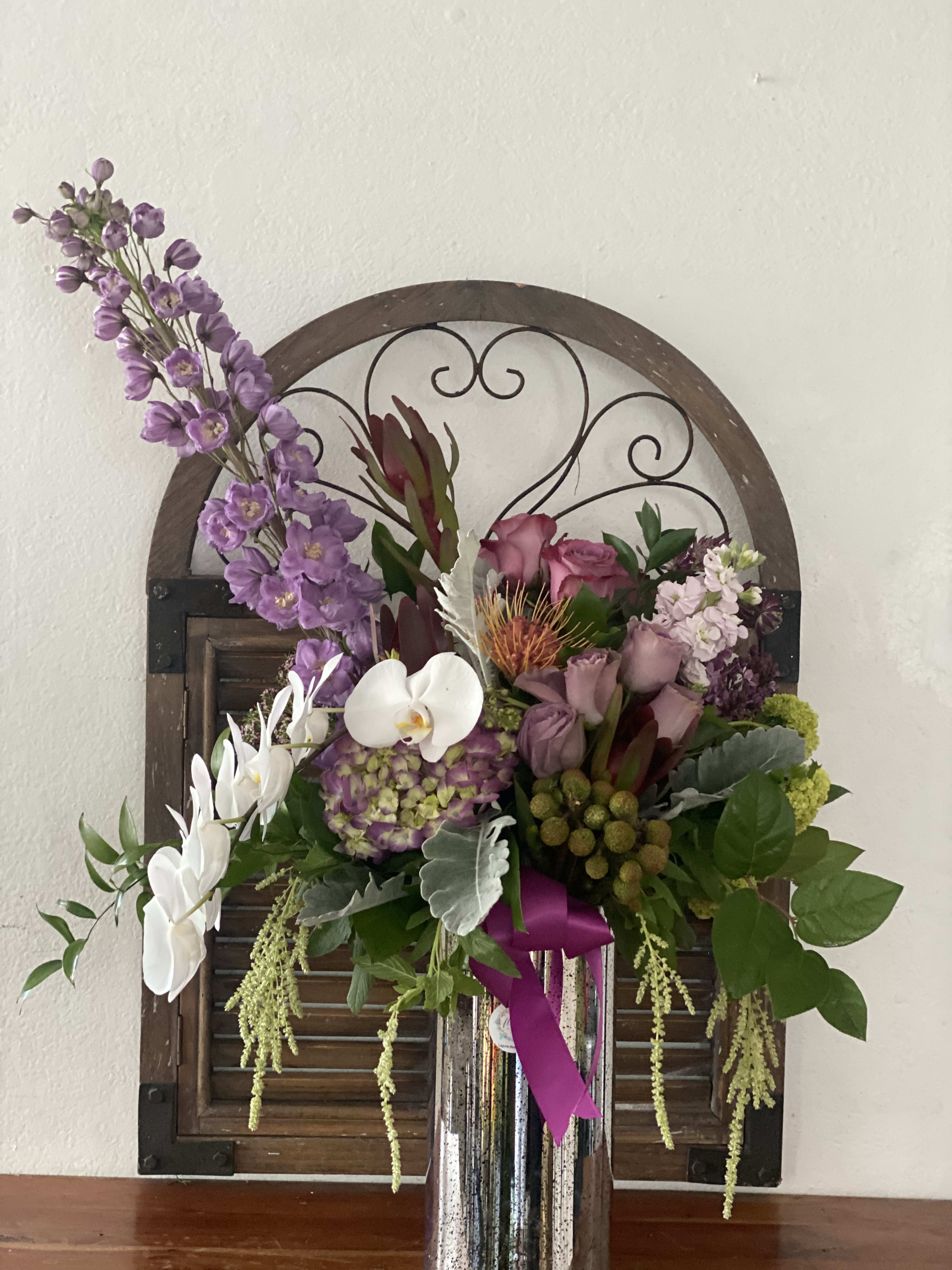 Purple and white floral arrangement in a tall silver vase