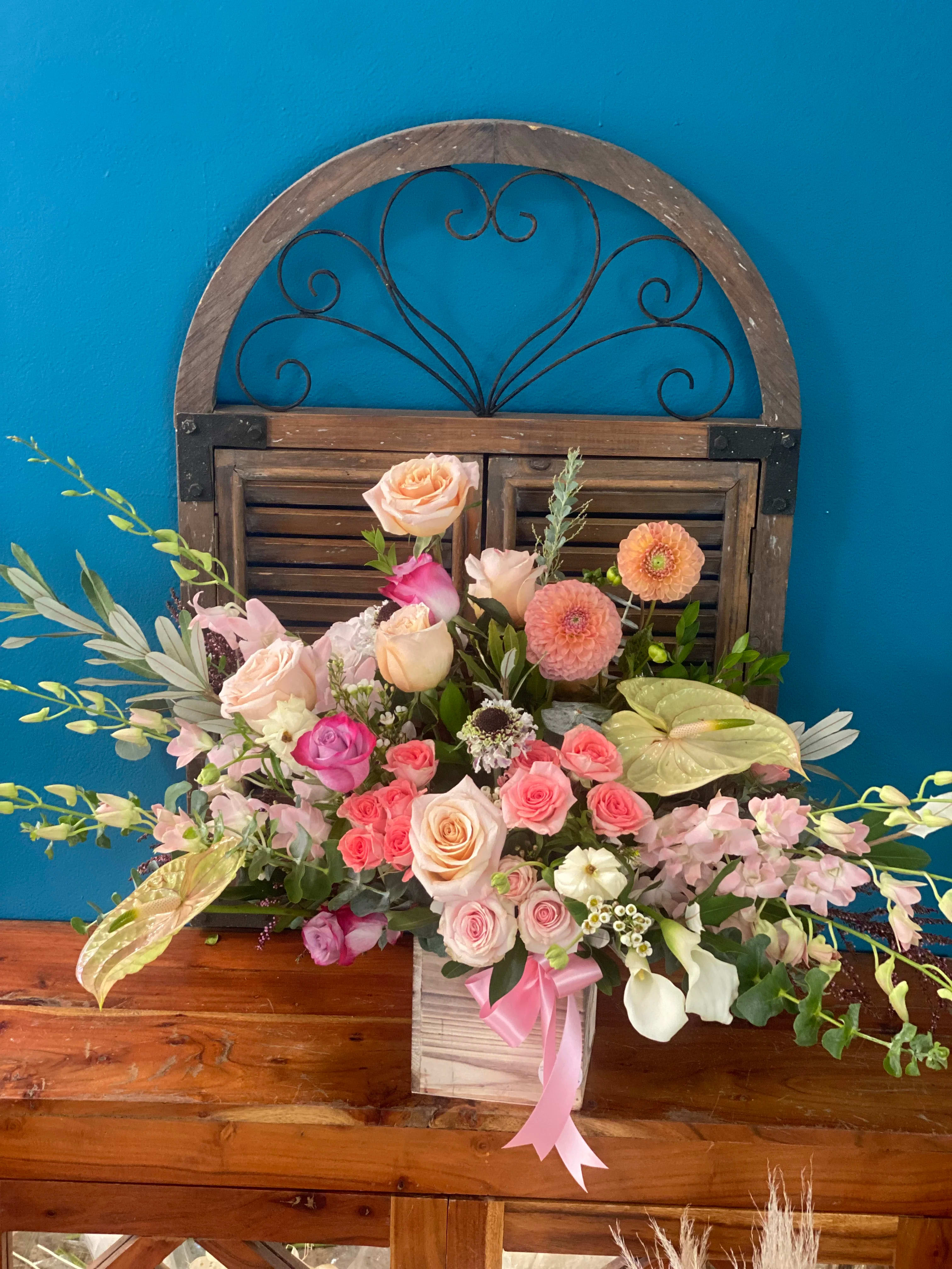 Mixed pink and peach floral arrangement in a wooden box with a pink ribbon