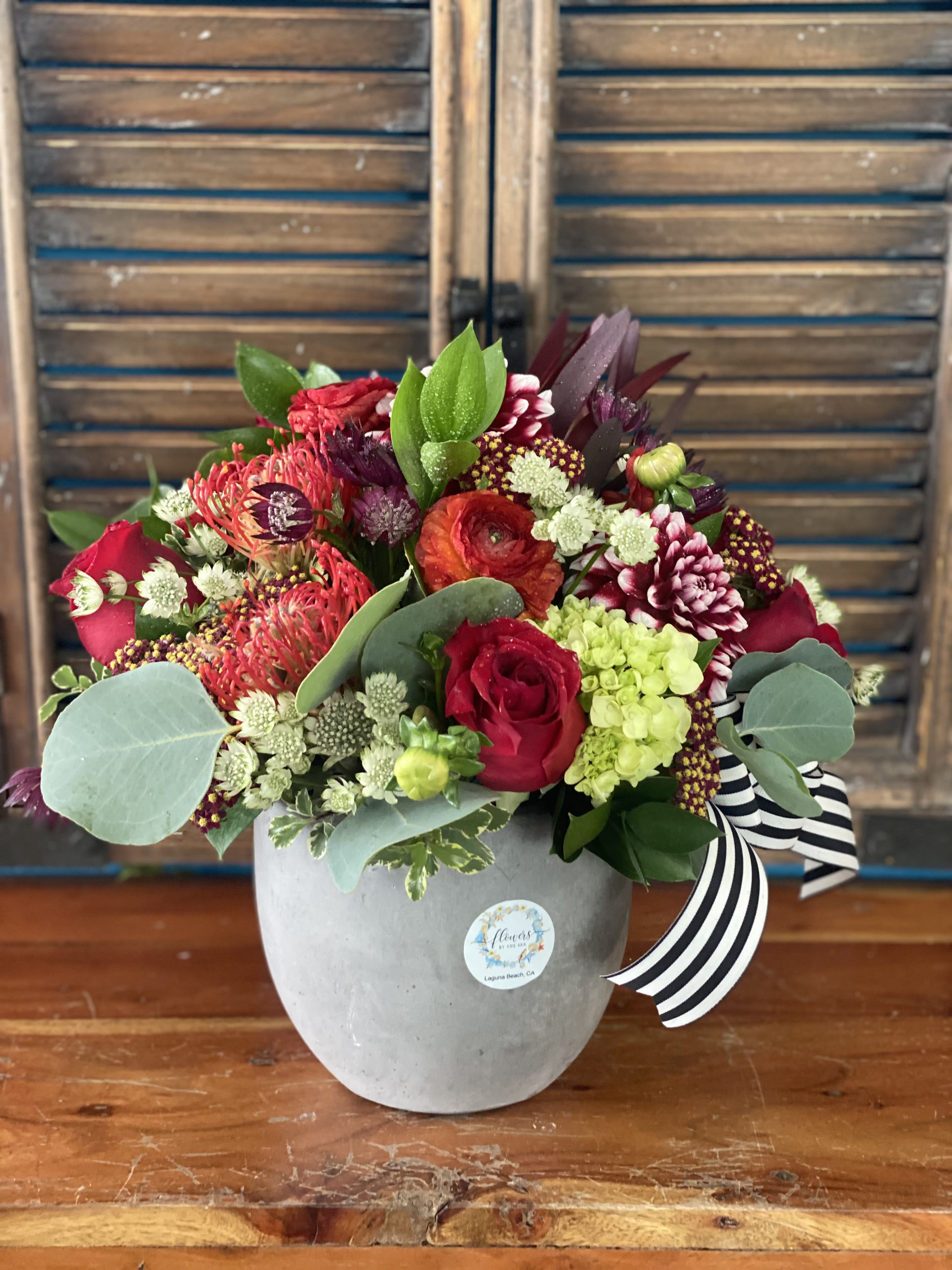 Mixed red and pink flower arrangement in a gray vase with a striped ribbon