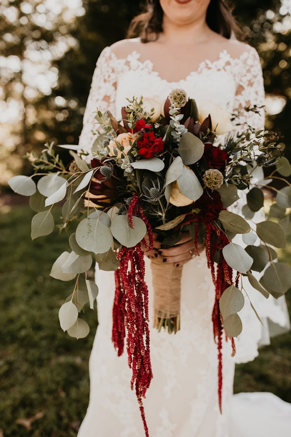 Bride holding a large bouquet with red flowers and trailing greenery