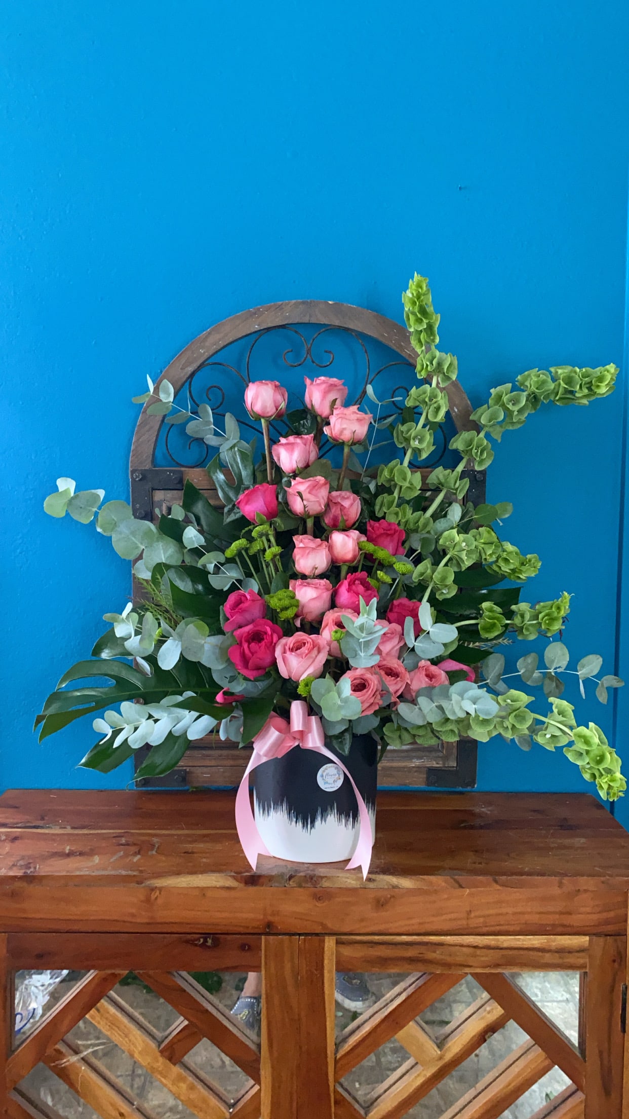 Pink rose arrangement in a white vase with a pink ribbon