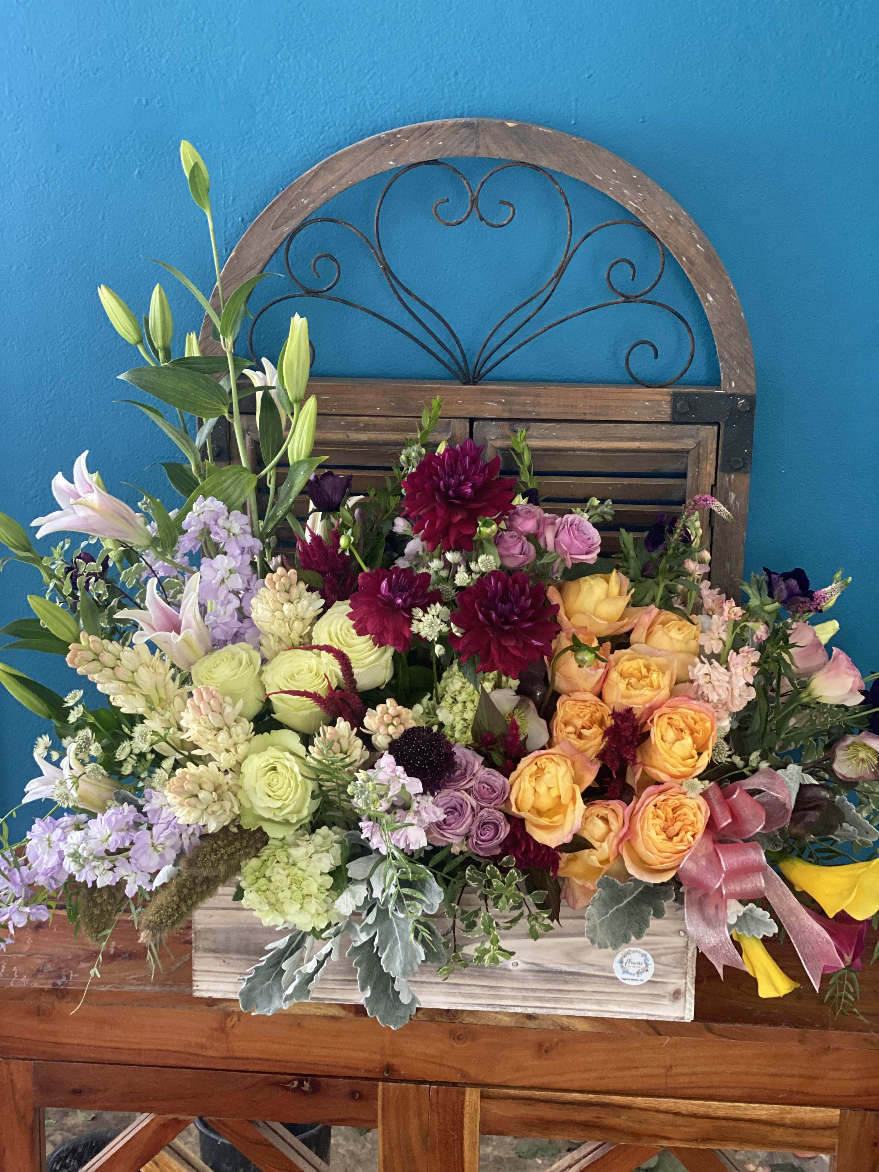 Large mixed flower arrangement in a wooden box with a pink ribbon