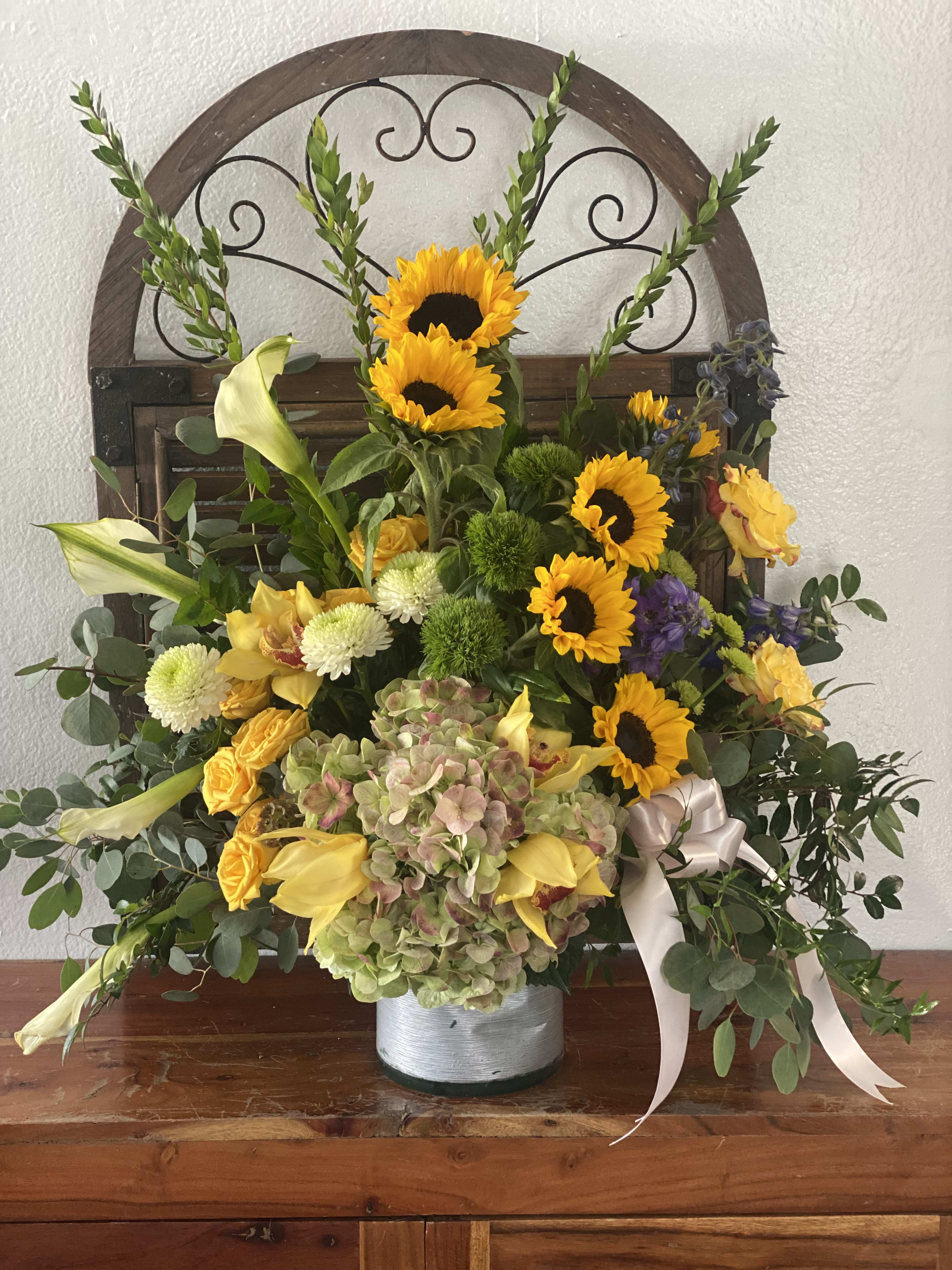 Mixed floral arrangement with sunflowers, lilies, and hydrangea in a metal container