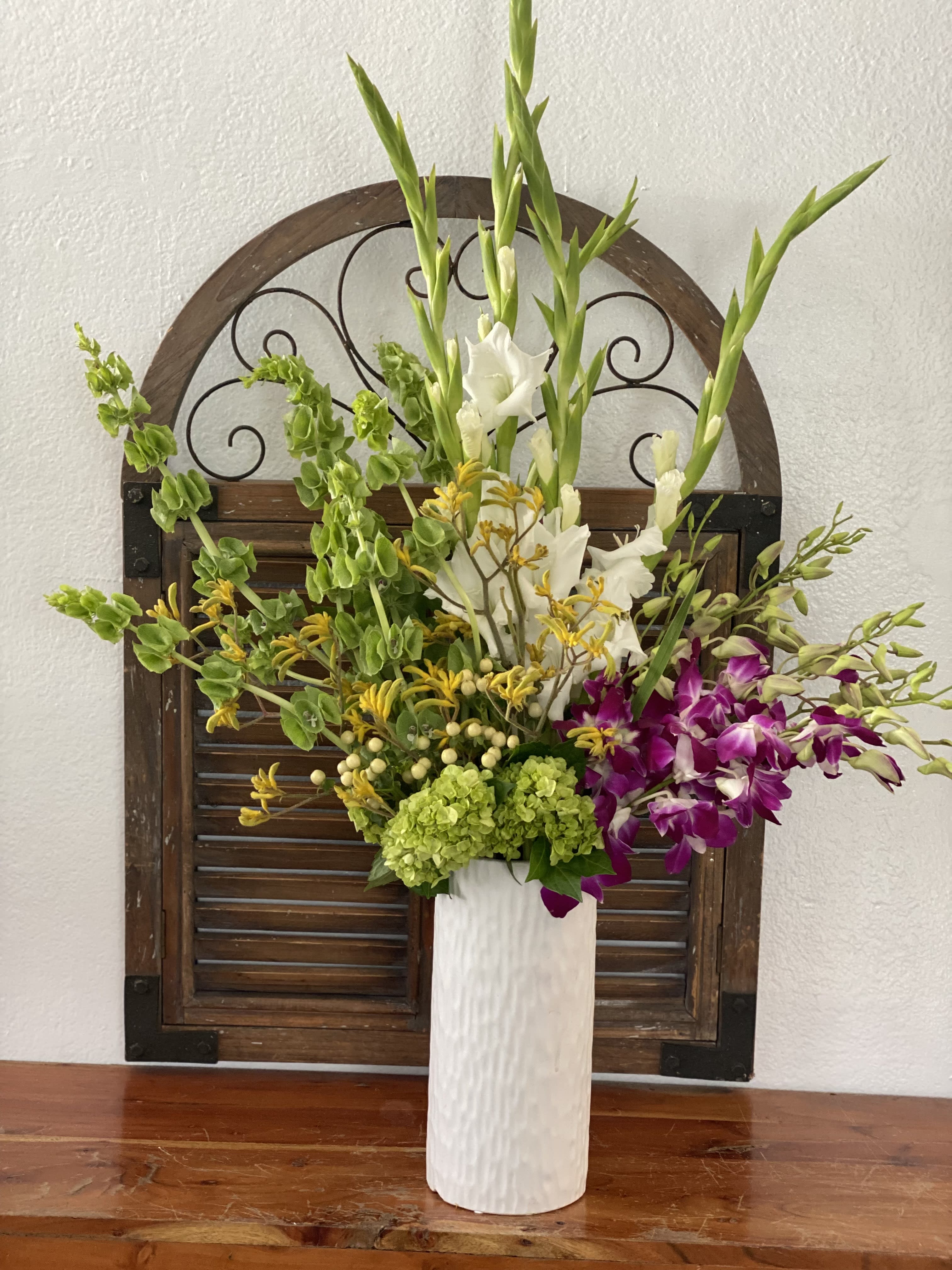 Tall floral arrangement in a white vase with white, green, yellow, and purple blooms