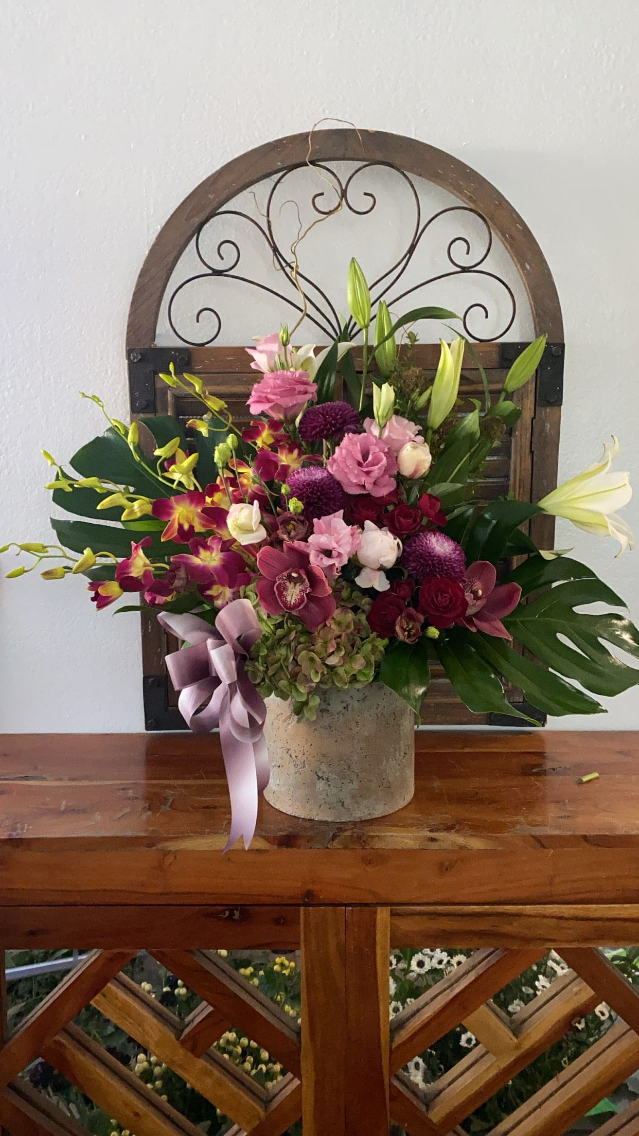 Mixed pink and purple floral arrangement in a stone vase with a ribbon