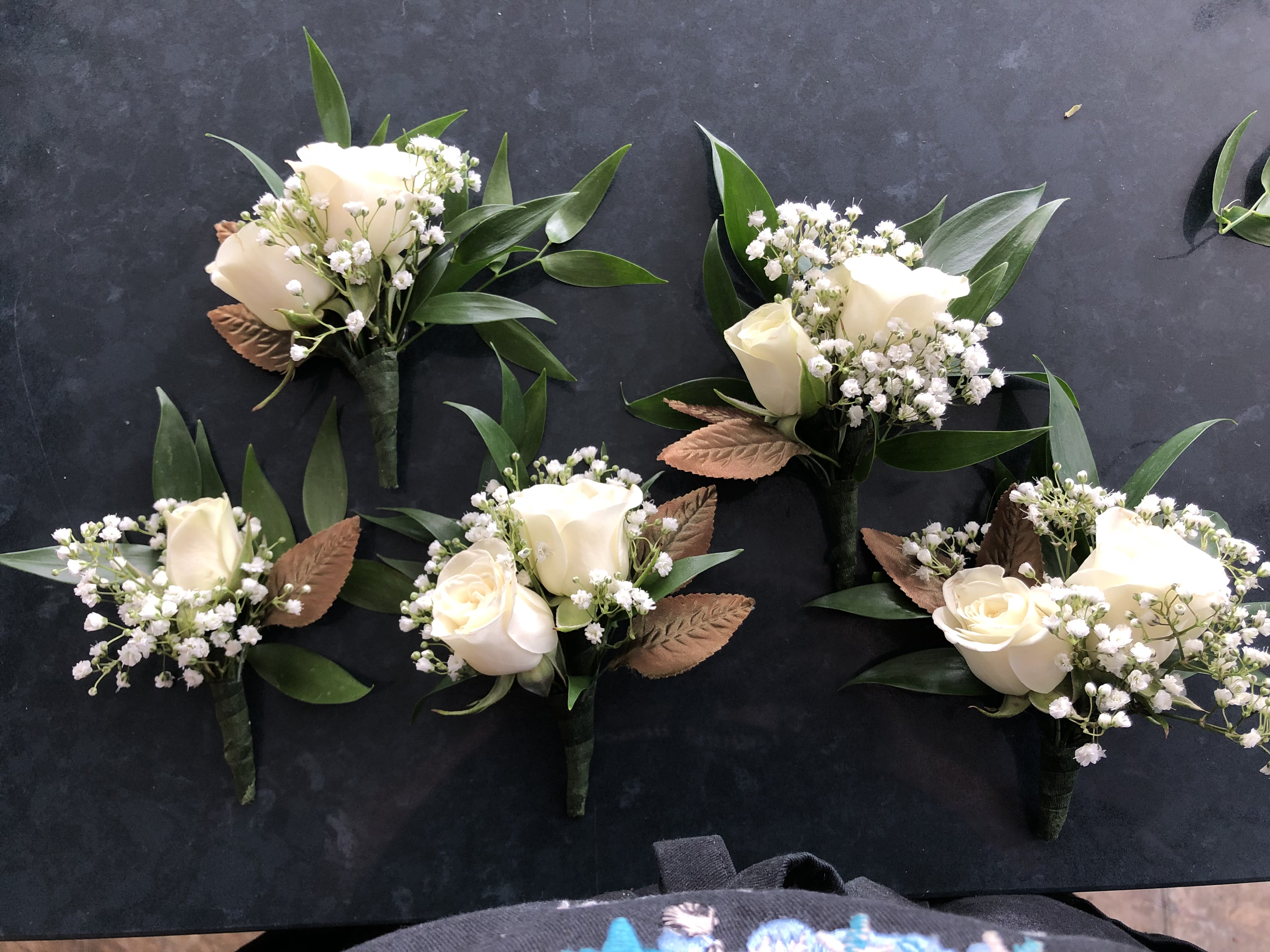 Small white rose boutonnieres with baby's breath and green leaves