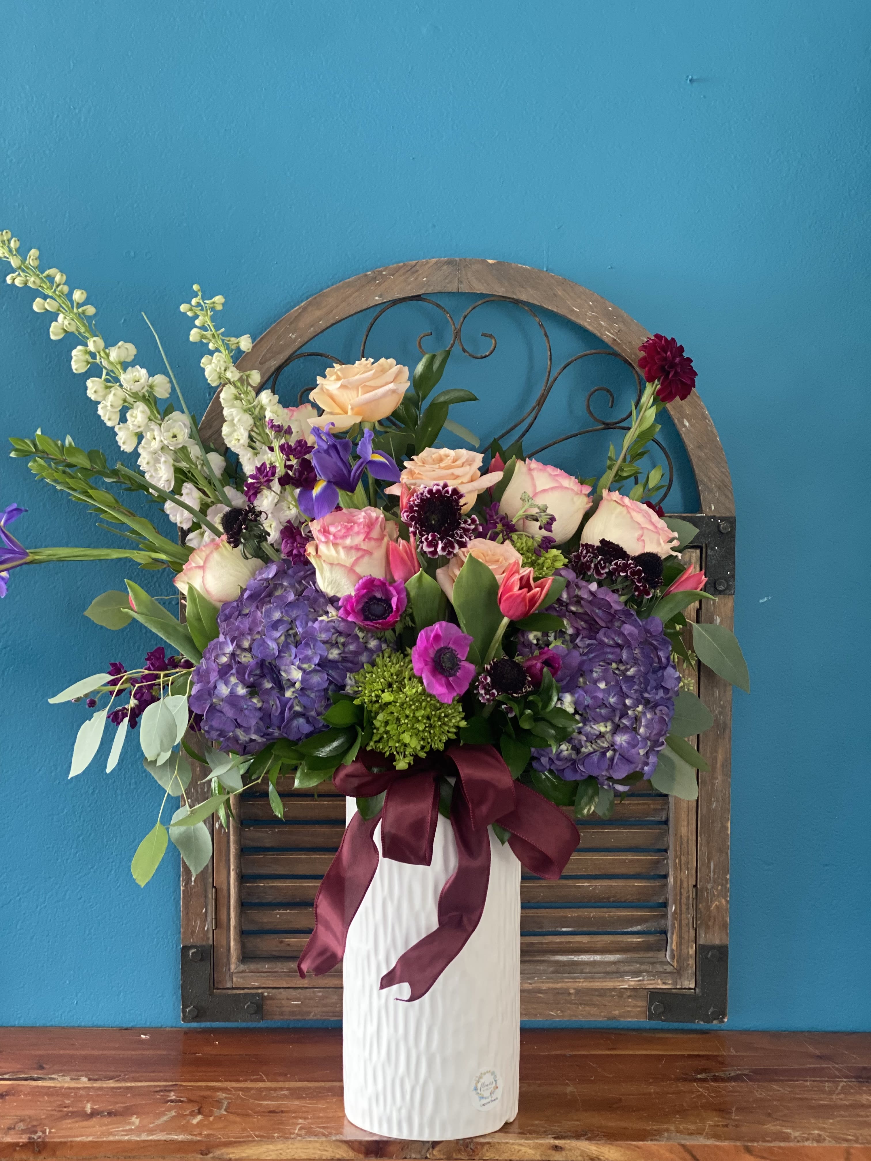 Tall floral arrangement in a white vase with purple, pink, and peach blooms