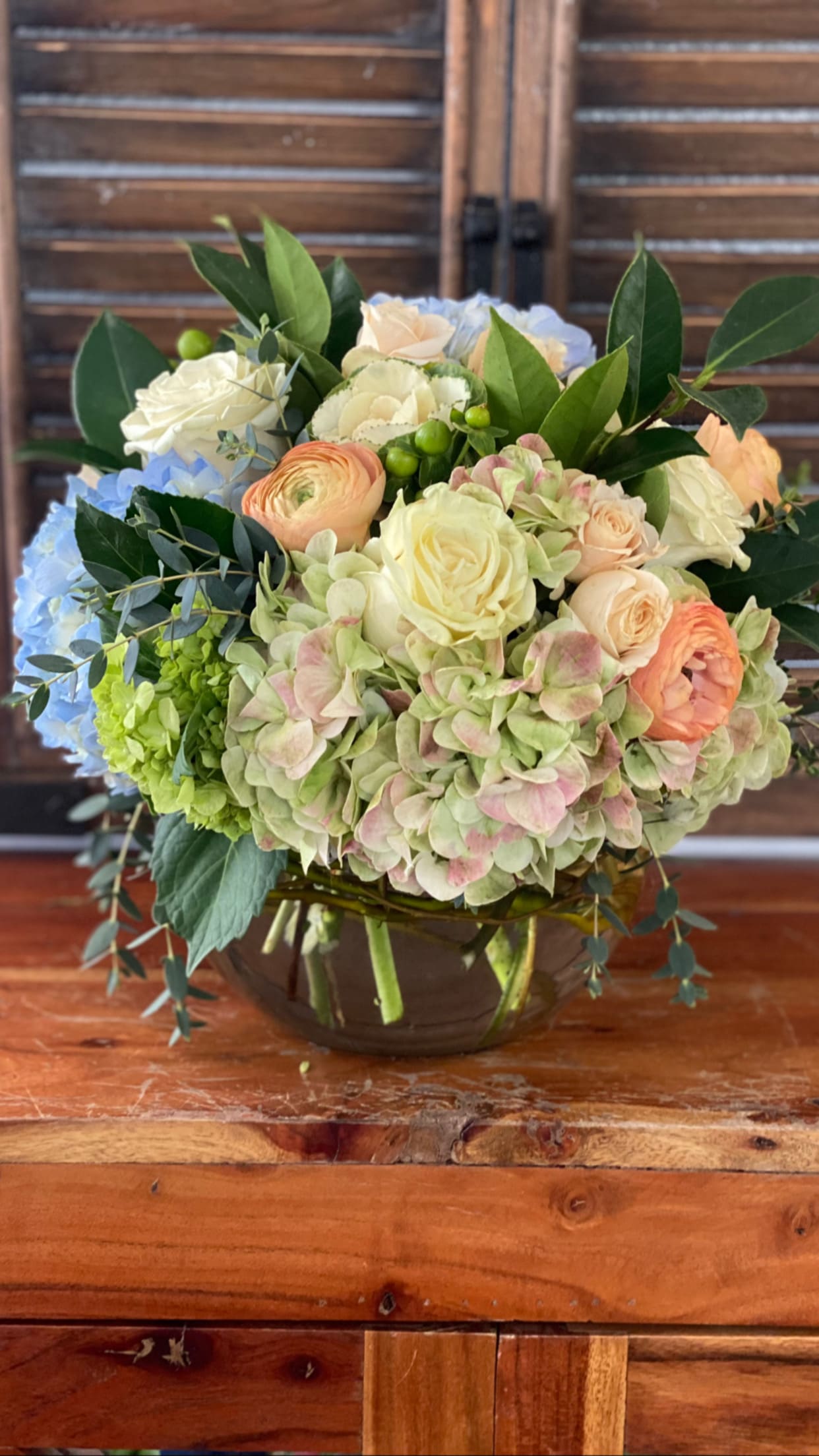 Mixed bouquet of pastel roses, hydrangeas, and ranunculus in a glass vase