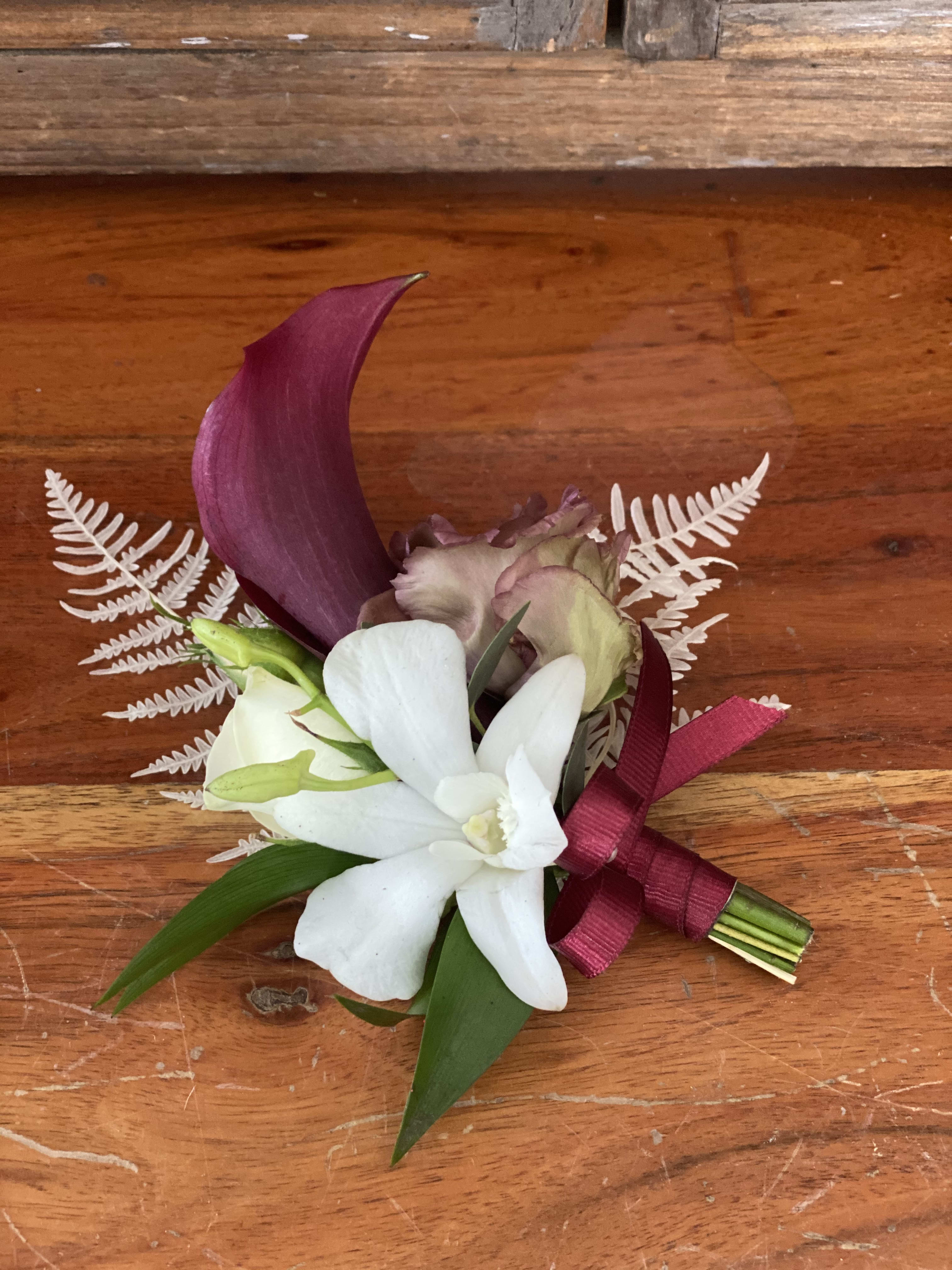 Small boutonniere with white and purple flowers tied with a burgundy ribbon