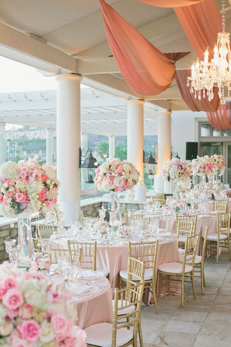 Pink and white floral centerpieces on round banquet tables with gold chairs