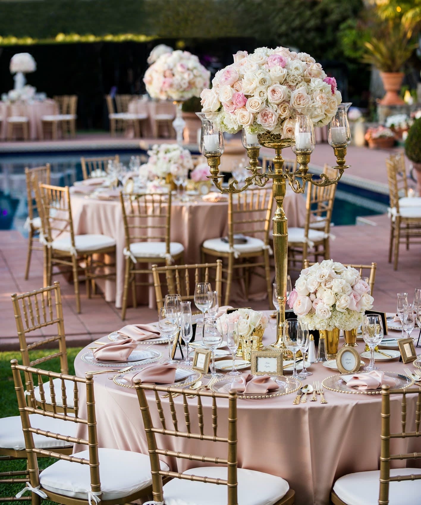 Blush and white rose centerpieces on gold stands at an outdoor table setting.