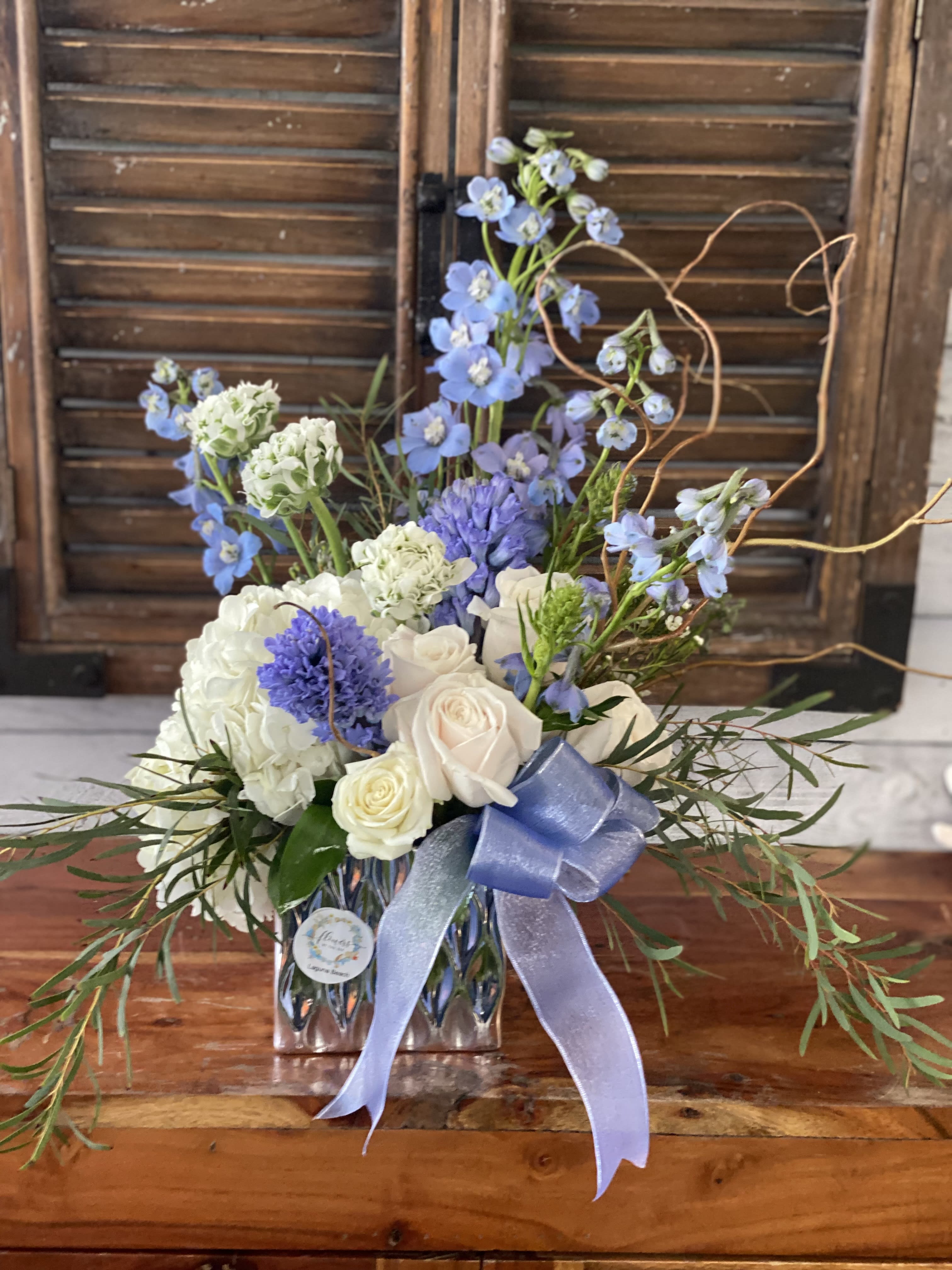 Blue and white floral arrangement in a glass vase with a ribbon
