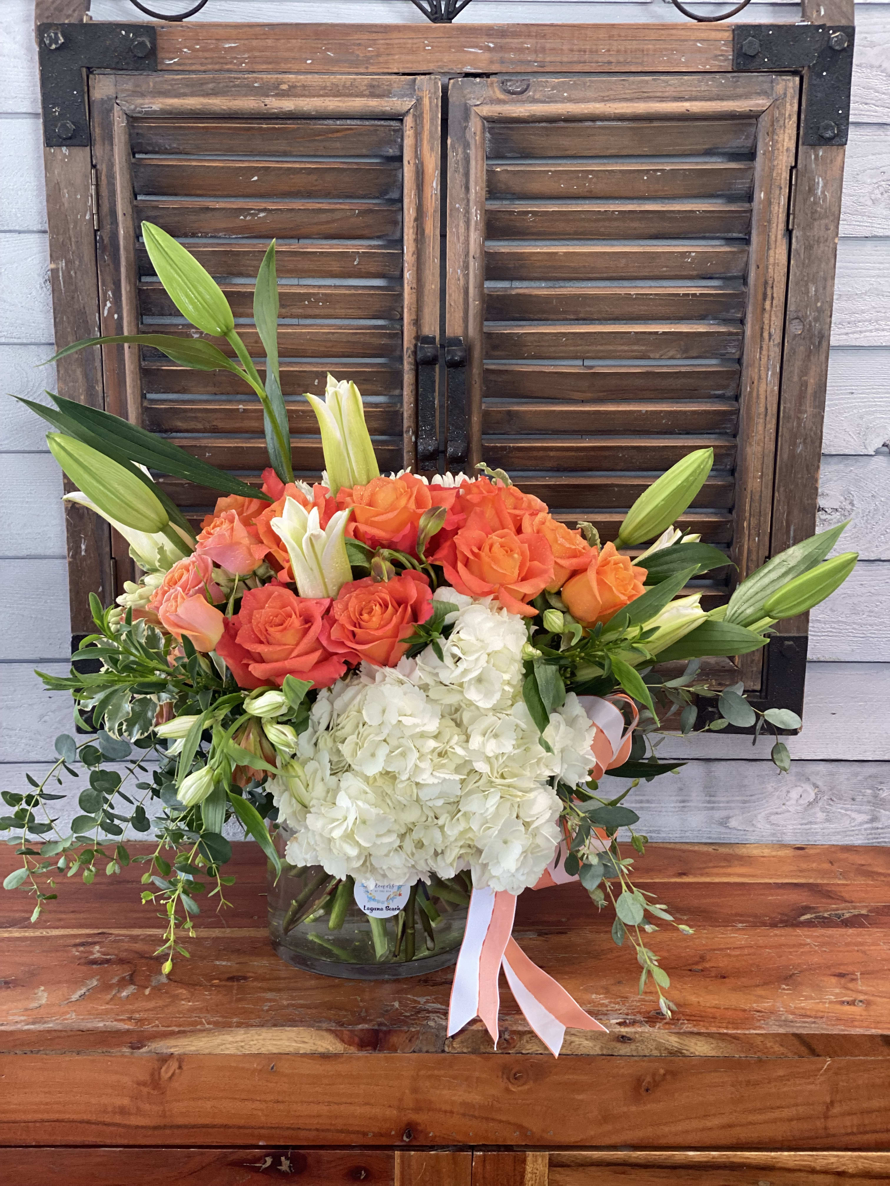 Bouquet of orange roses, white hydrangeas, and lilies in a glass vase