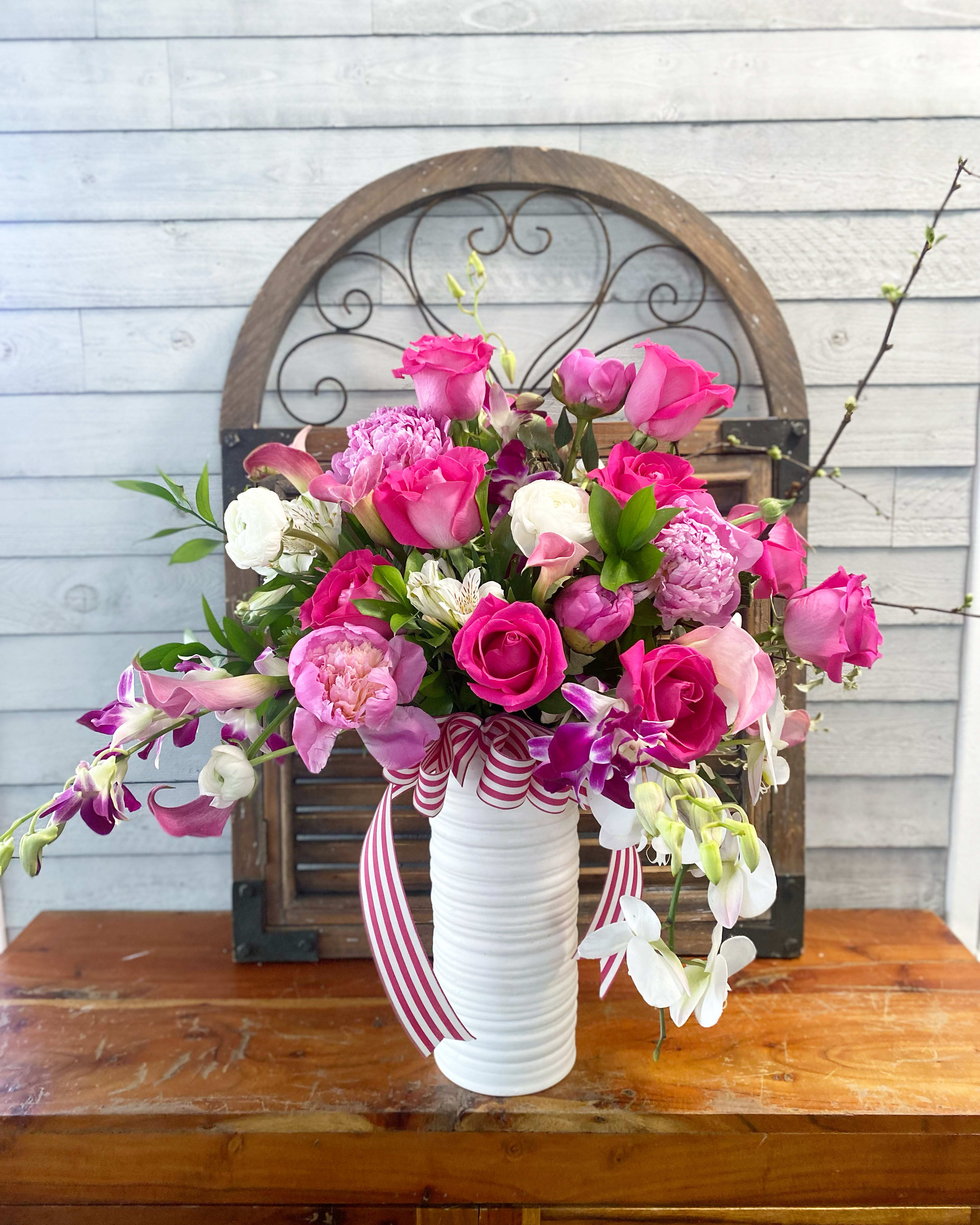 Pink and white floral arrangement in a white vase with striped ribbon