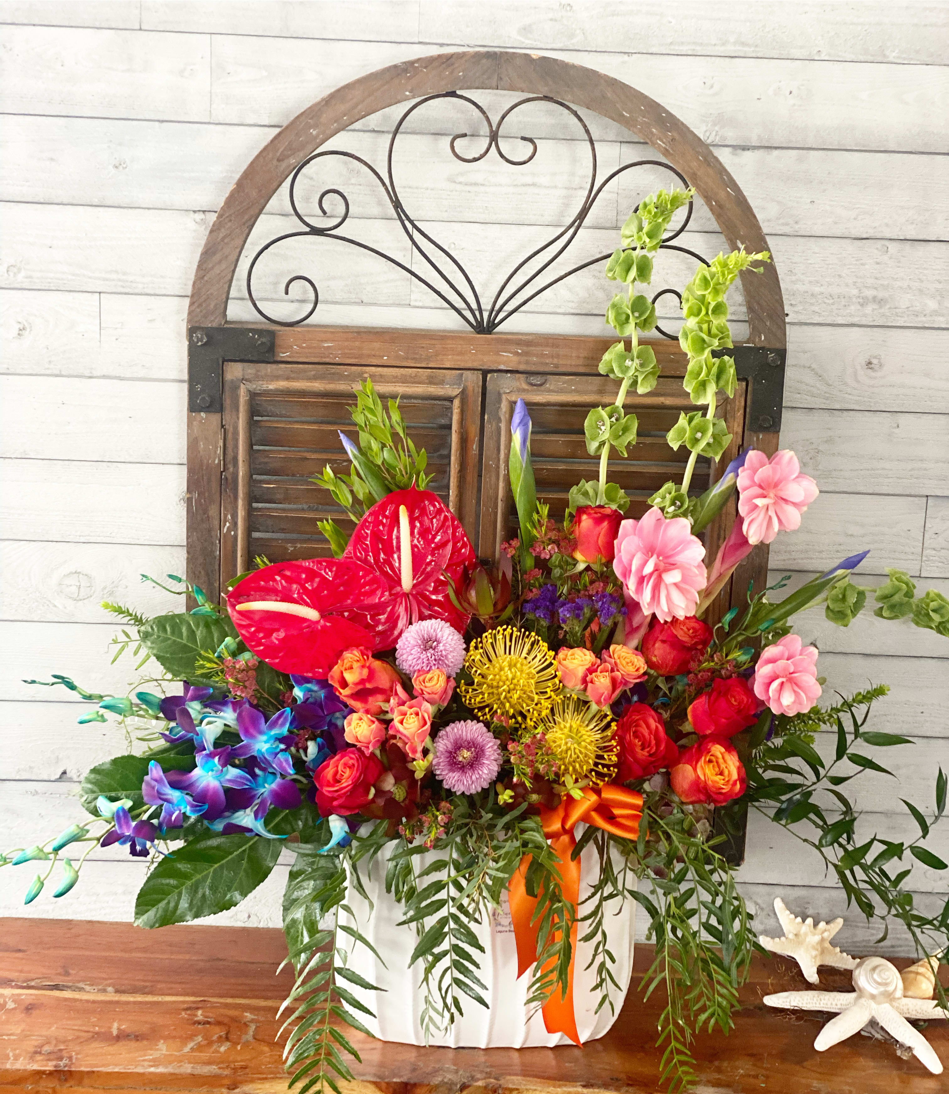 Colorful mixed flower arrangement in a white container with an orange ribbon
