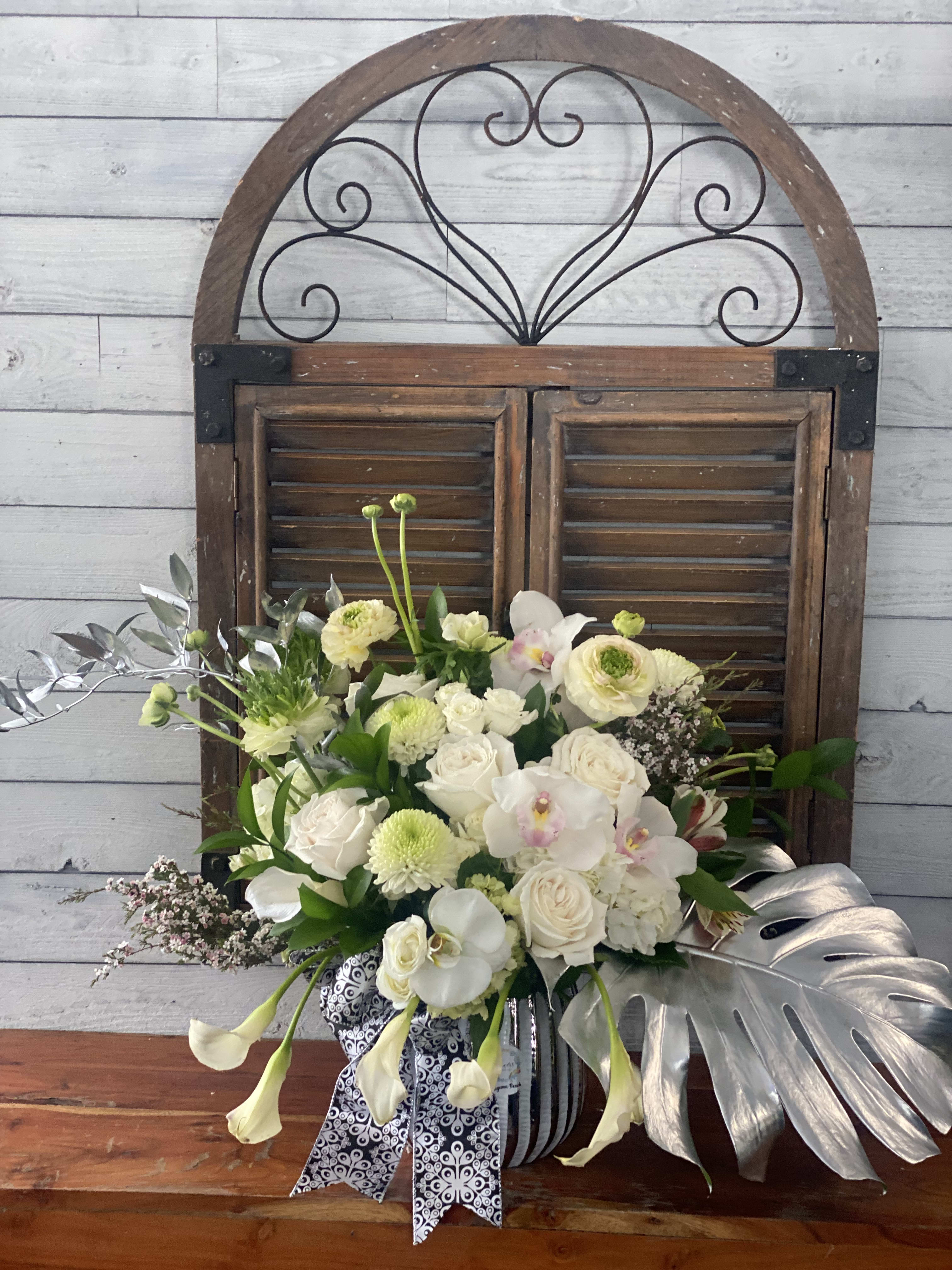 White and pale green floral arrangement in a striped vase with silver leaves