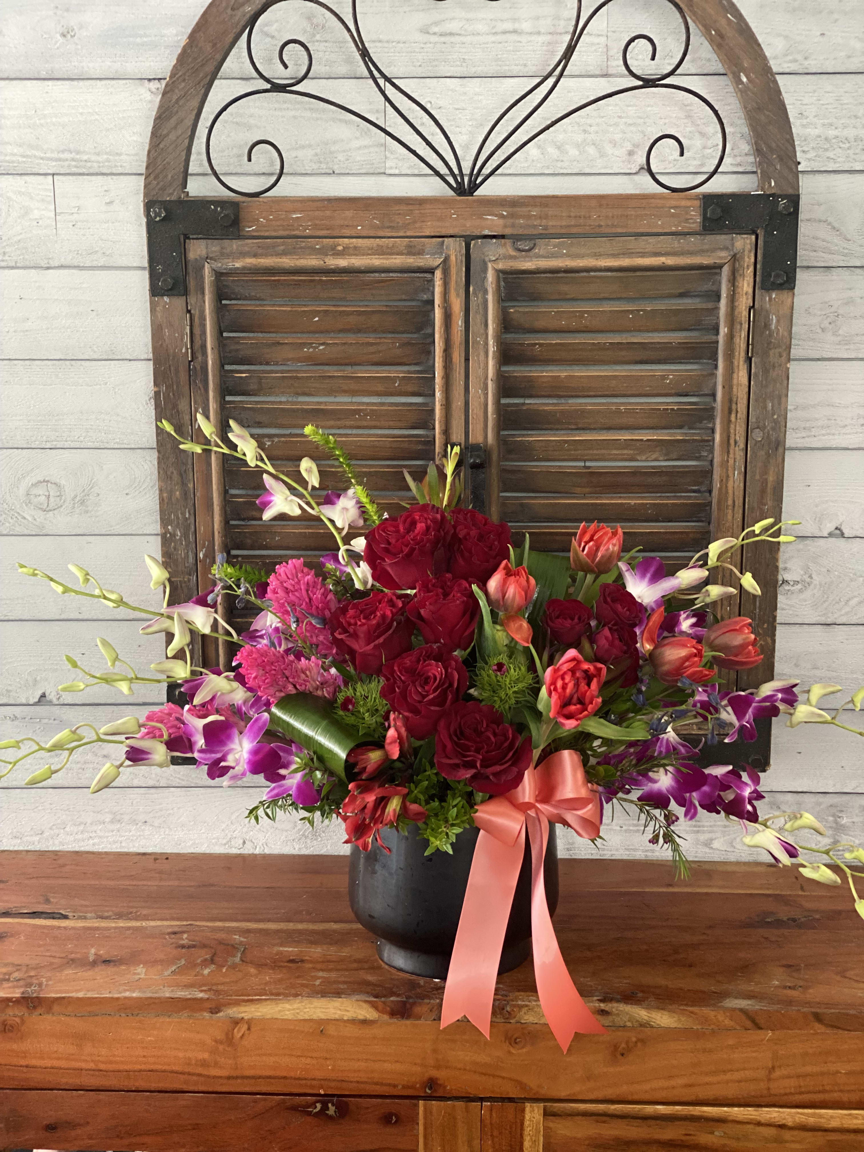 Bouquet of red roses and purple orchids in a black vase with a pink ribbon