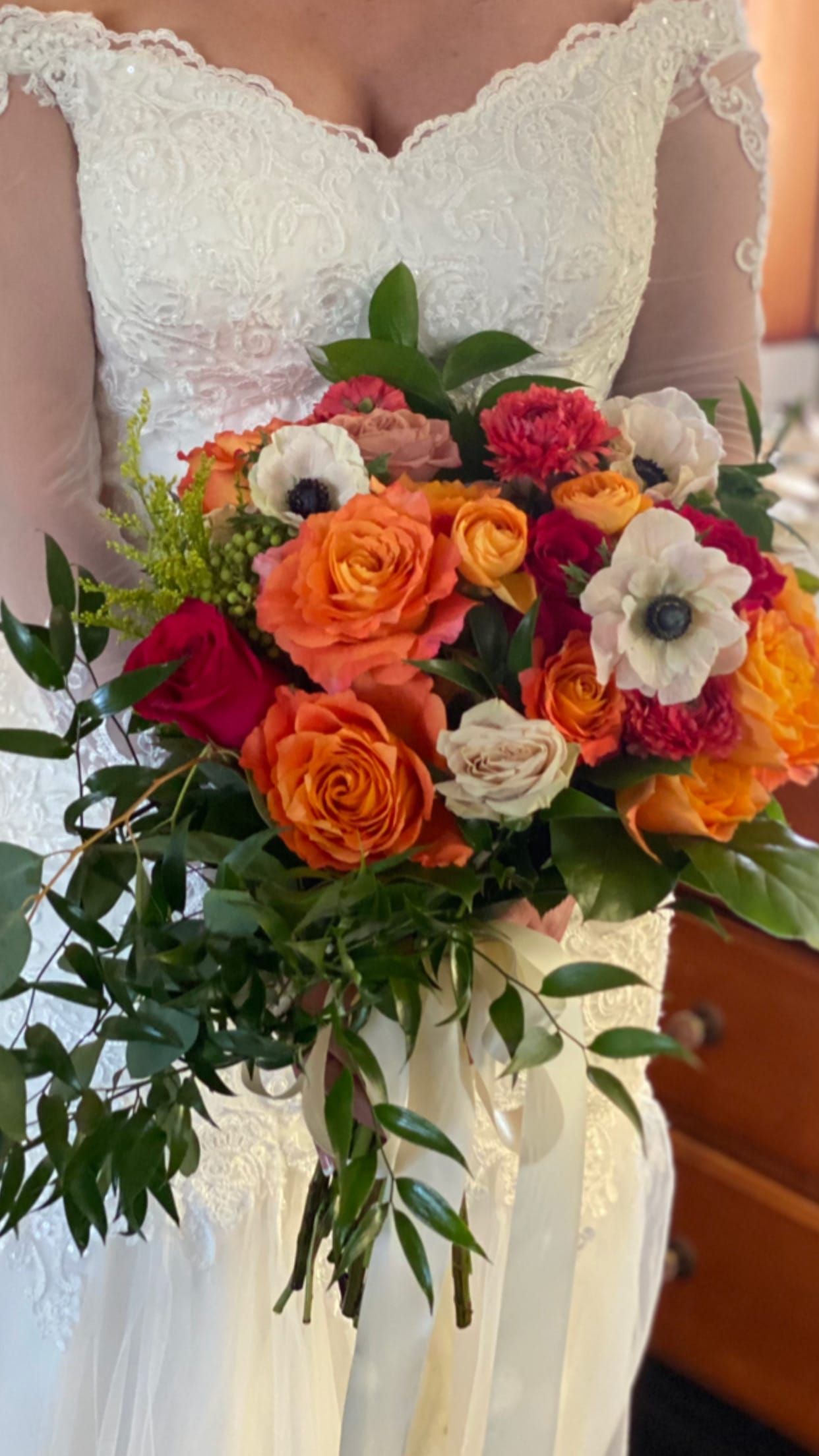 Bride holding a bouquet of orange, pink, and white flowers with trailing ribbon