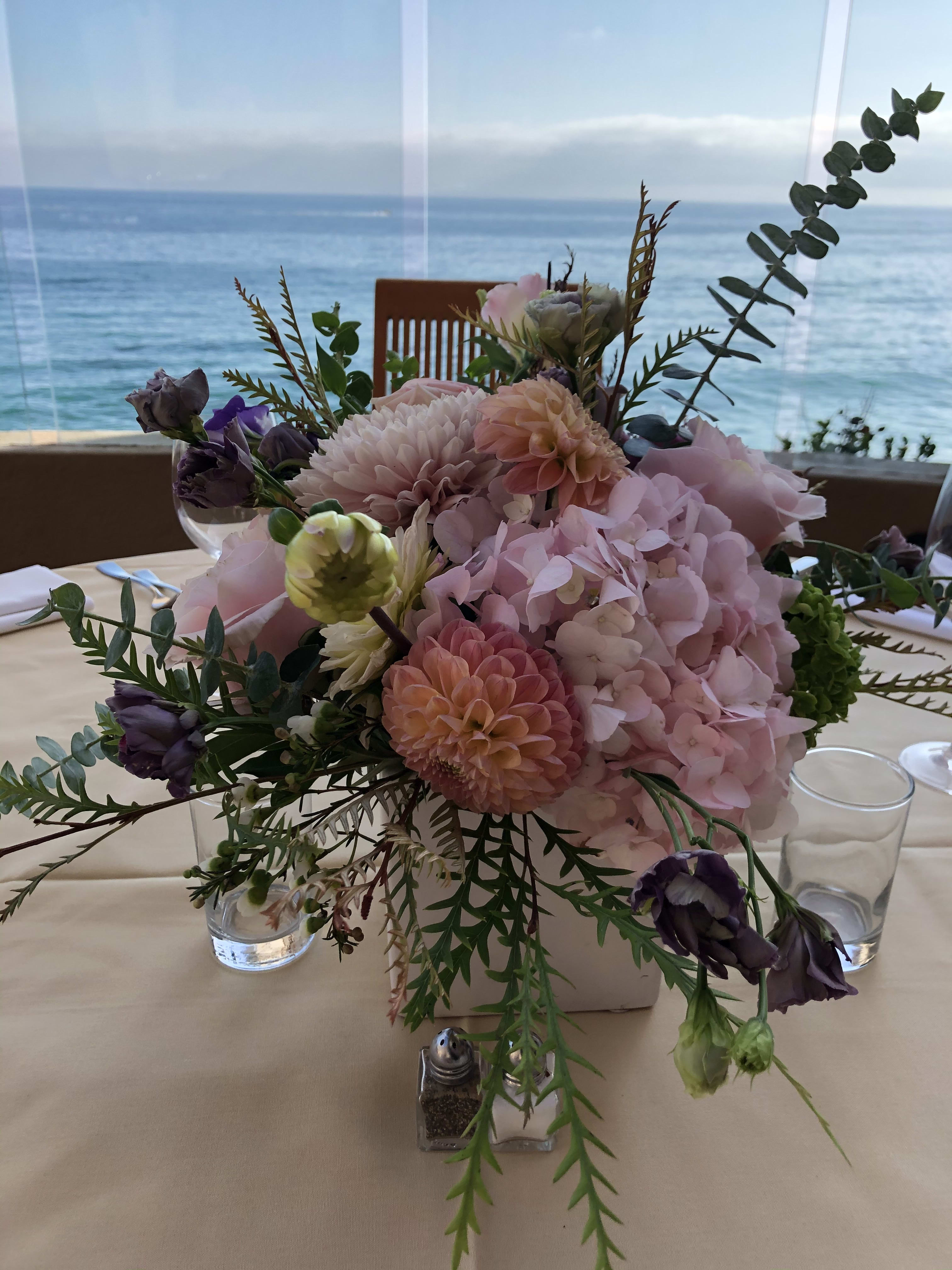 Pastel floral centerpiece in a low square vase on a table by the water