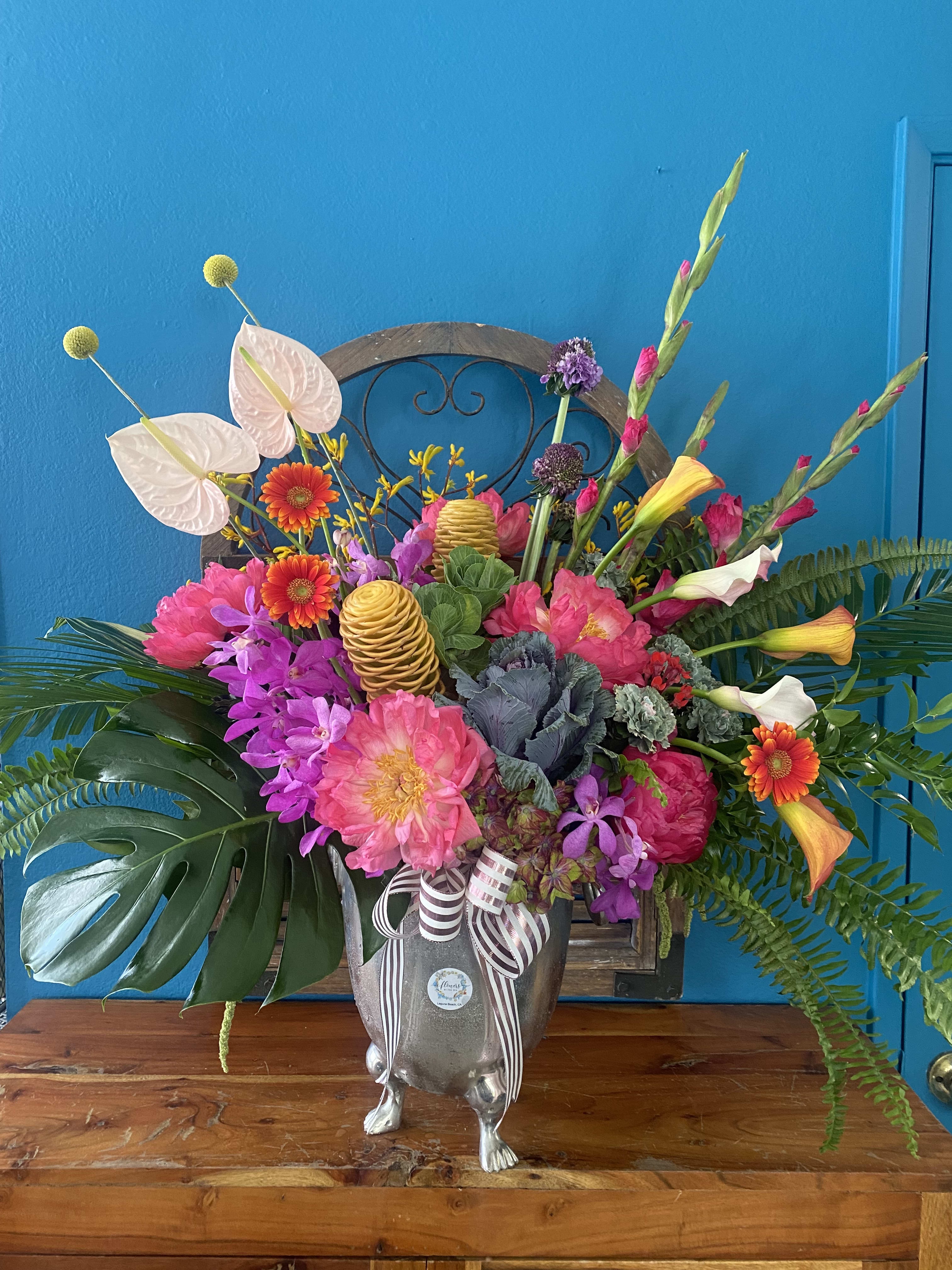 Large tropical floral arrangement in a silver urn with pink, purple, and orange blooms