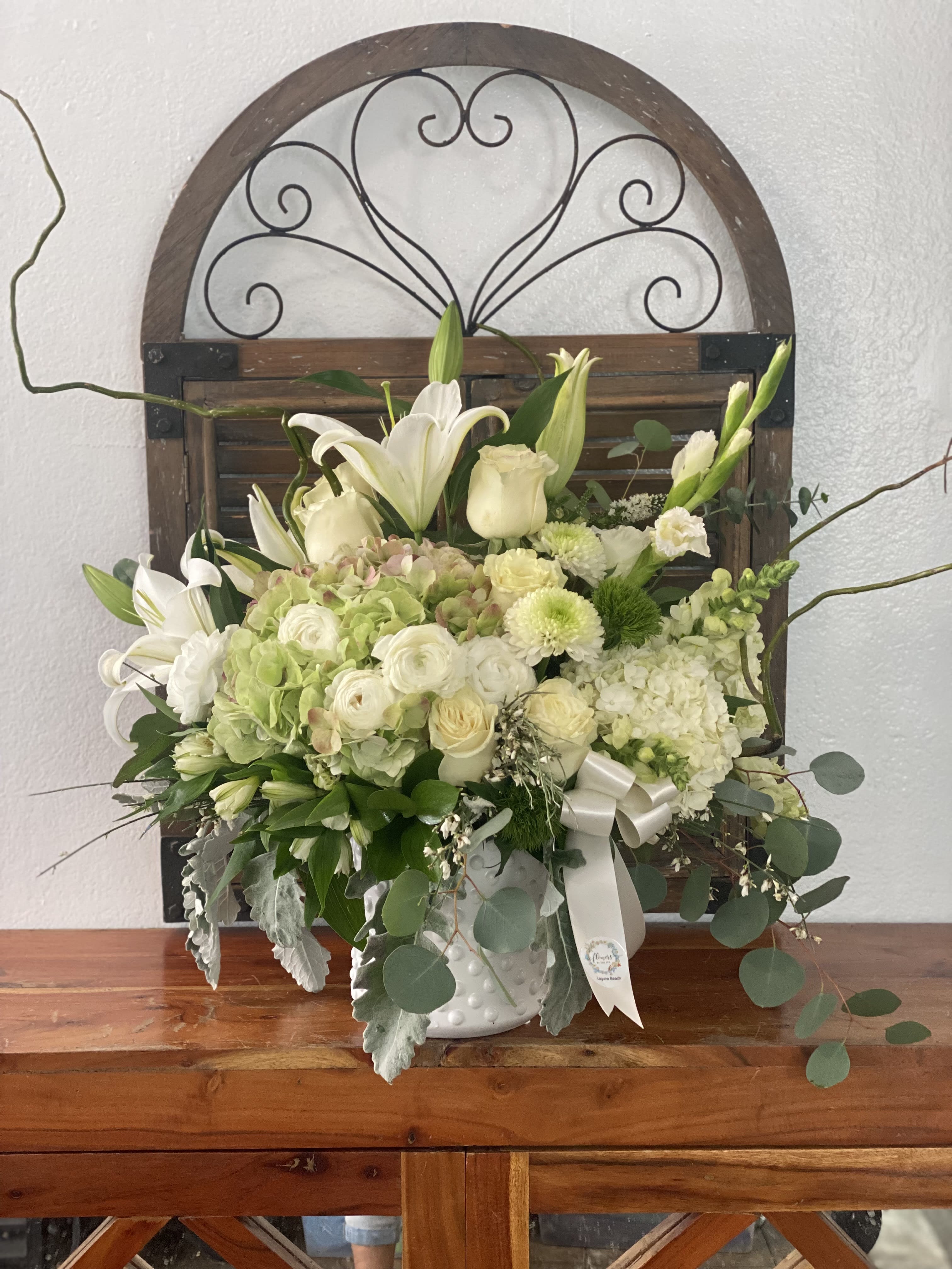 White floral arrangement in a white vase with lilies and roses