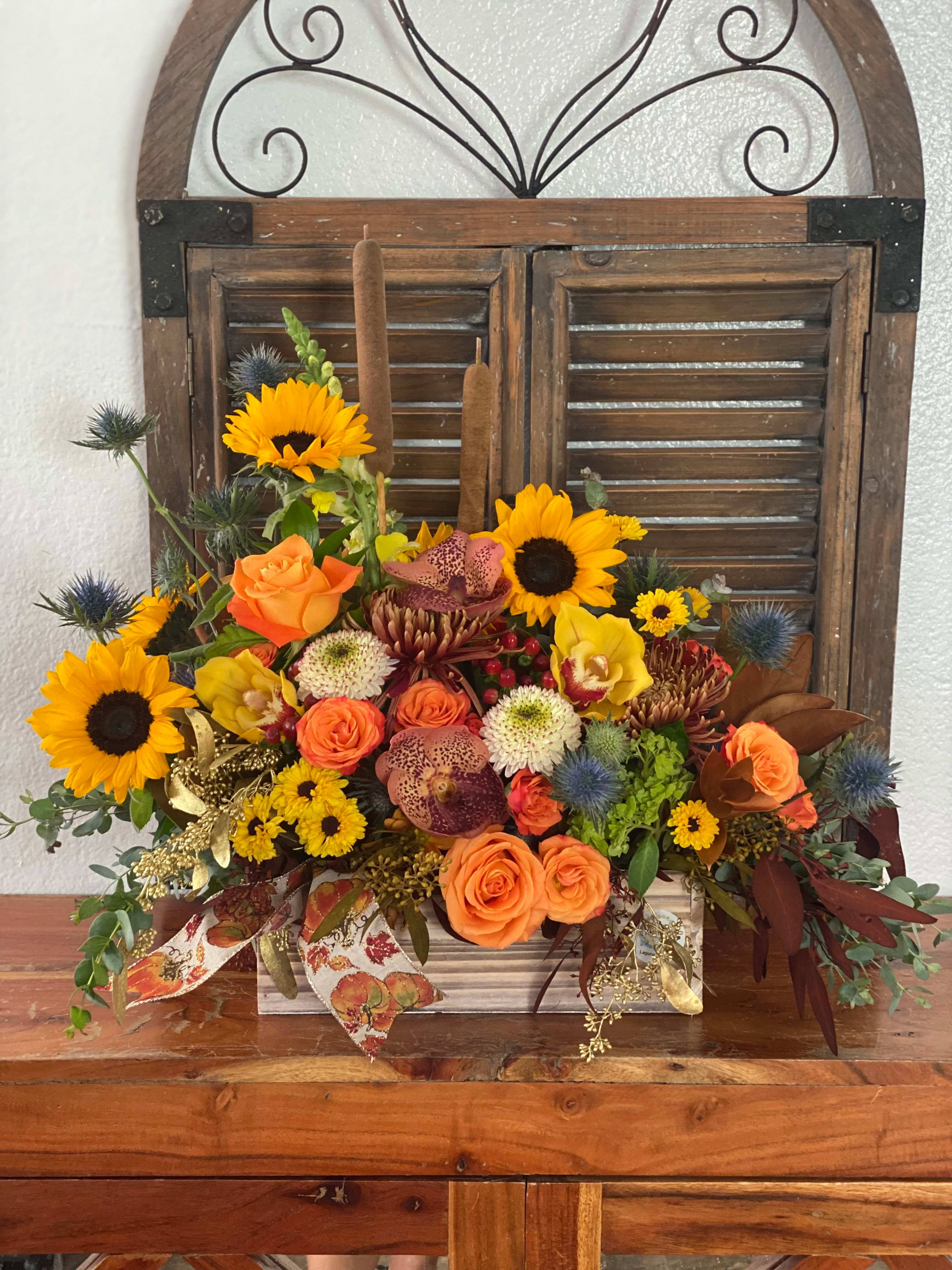 Mixed bouquet with sunflowers, orange roses, and orchids in a wooden container