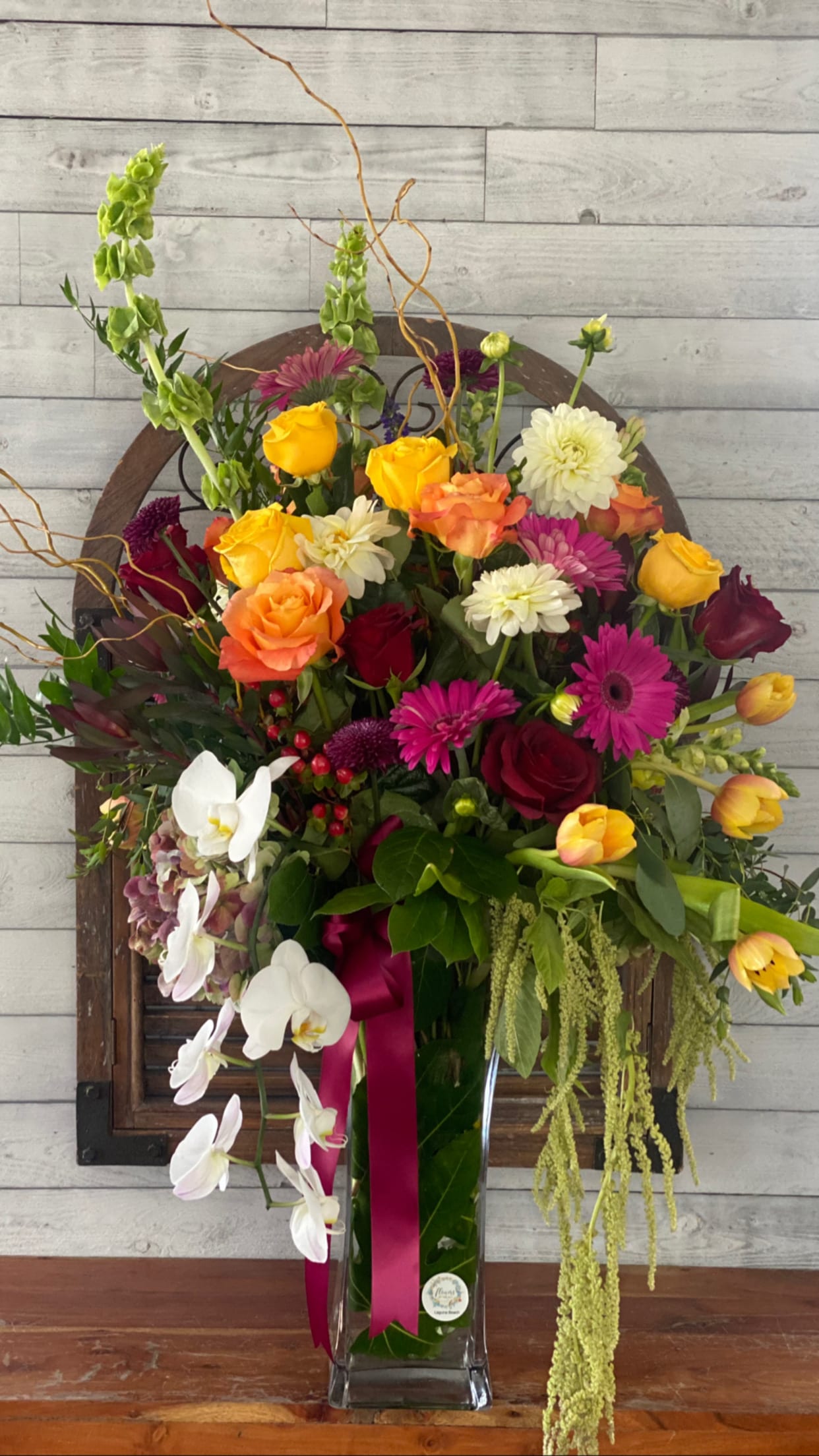Mixed bouquet in a tall glass vase with roses, orchids, and bright daisies