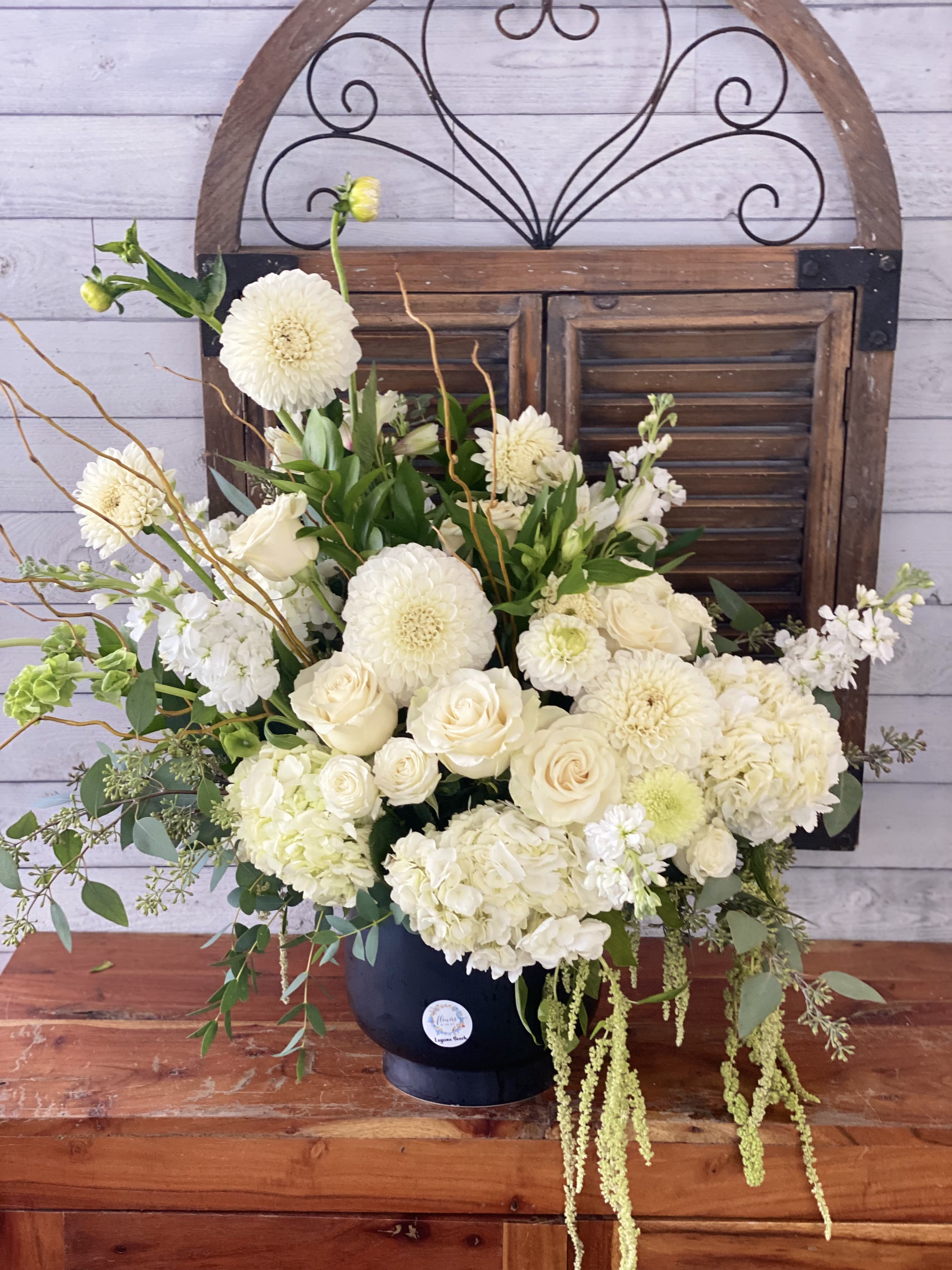 Cream floral arrangement in a dark vase with roses, dahlias, and hydrangeas