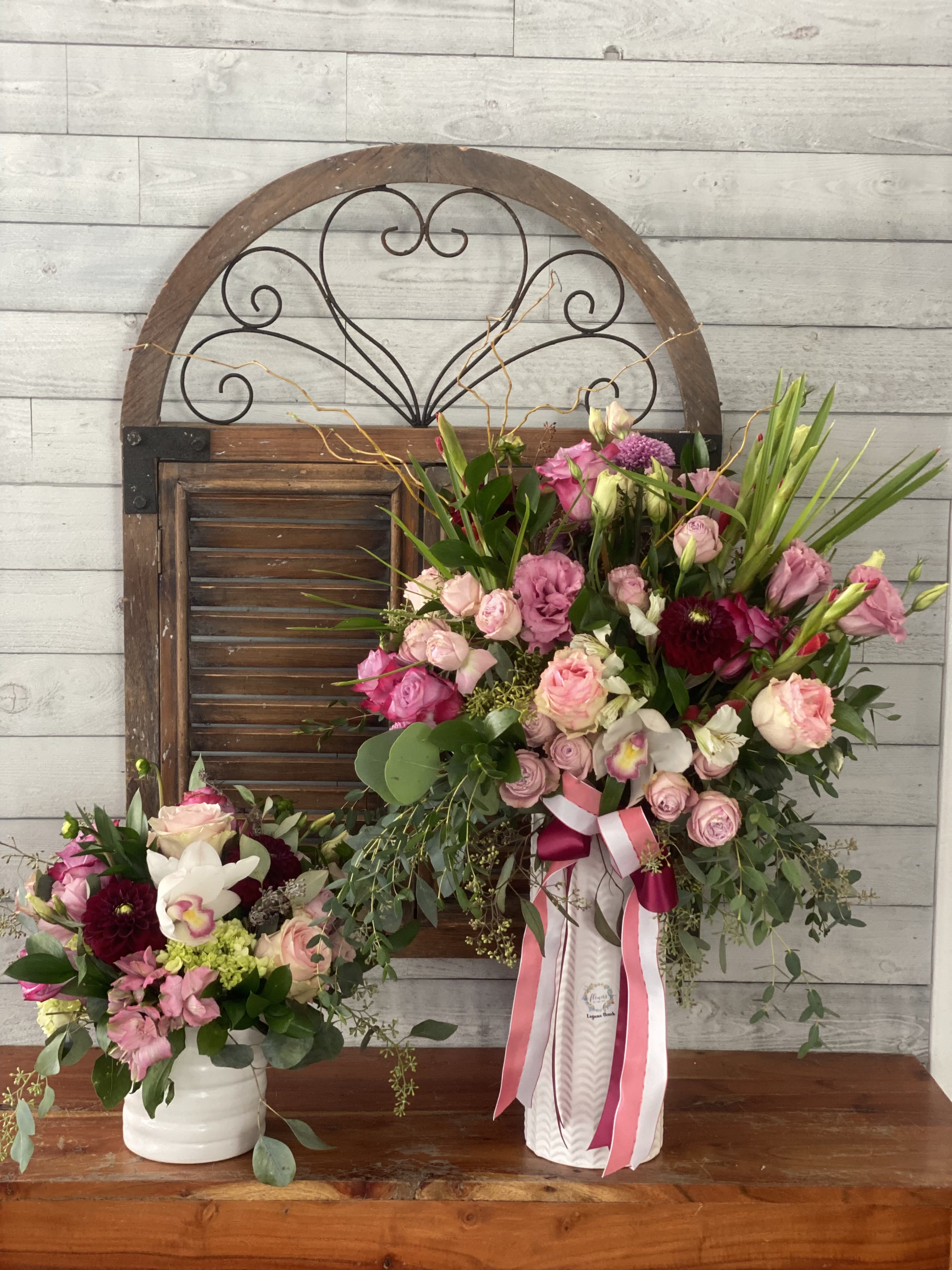 Two pink floral arrangements in white vases with ribbon accents