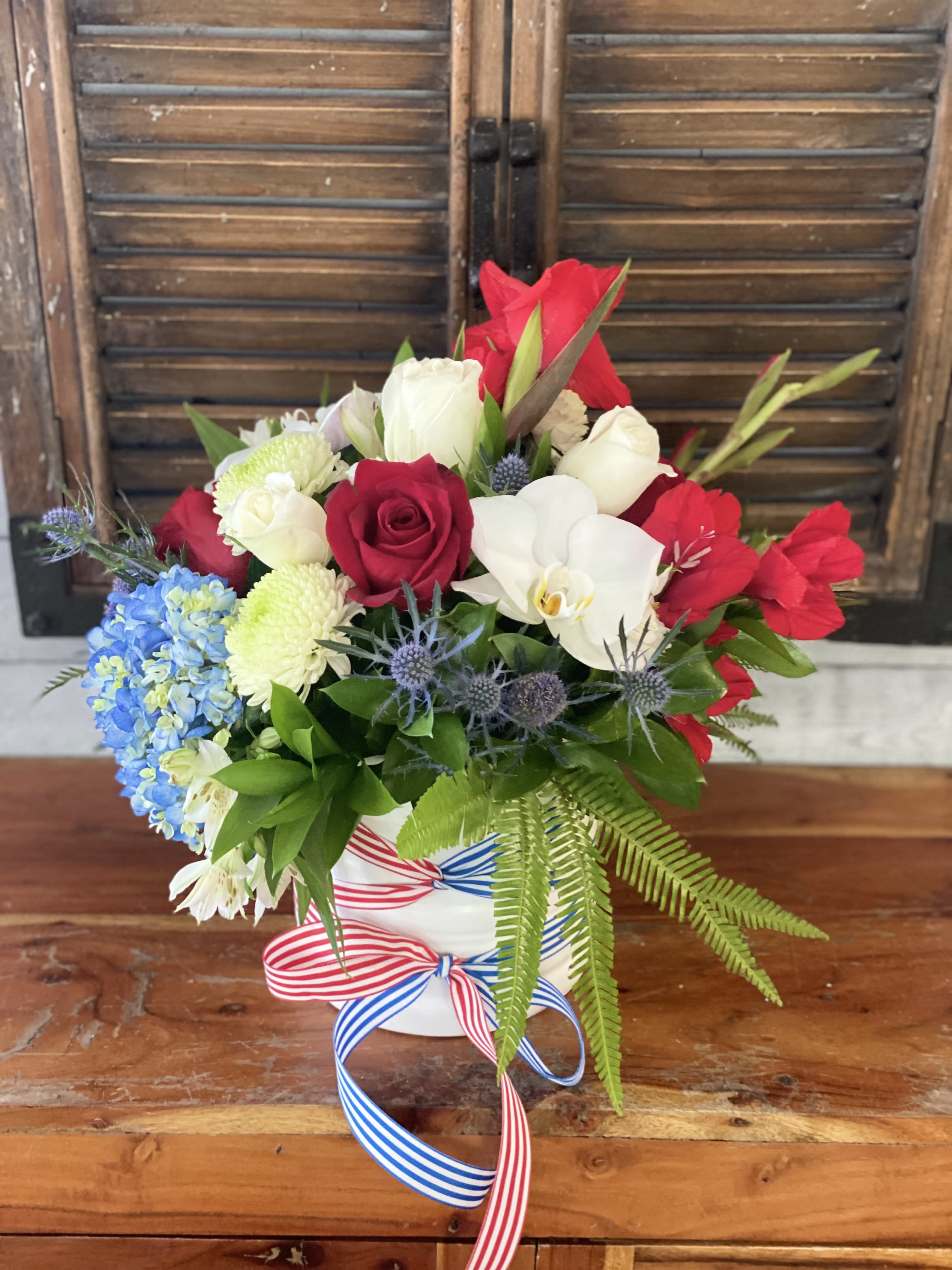Red, white, and blue floral arrangement in a white vase with ribbon