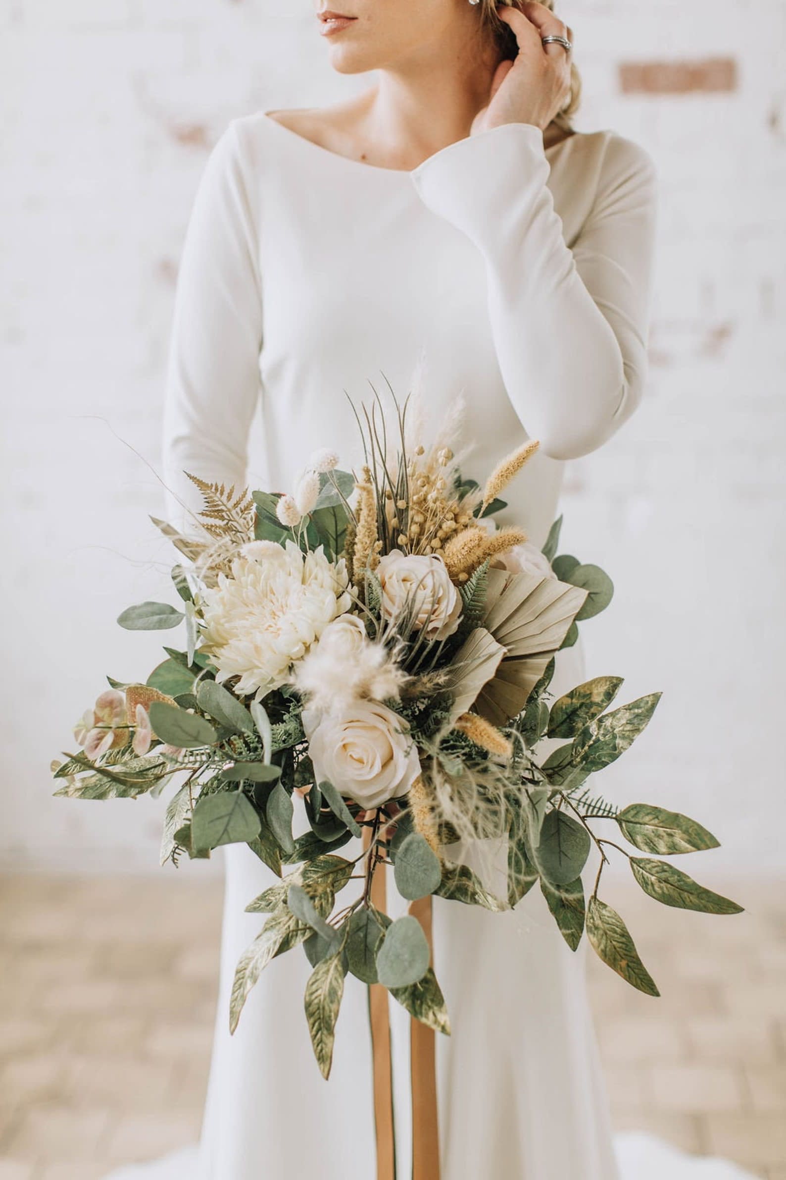 Bride holding a cream and green bouquet with roses and dried grasses