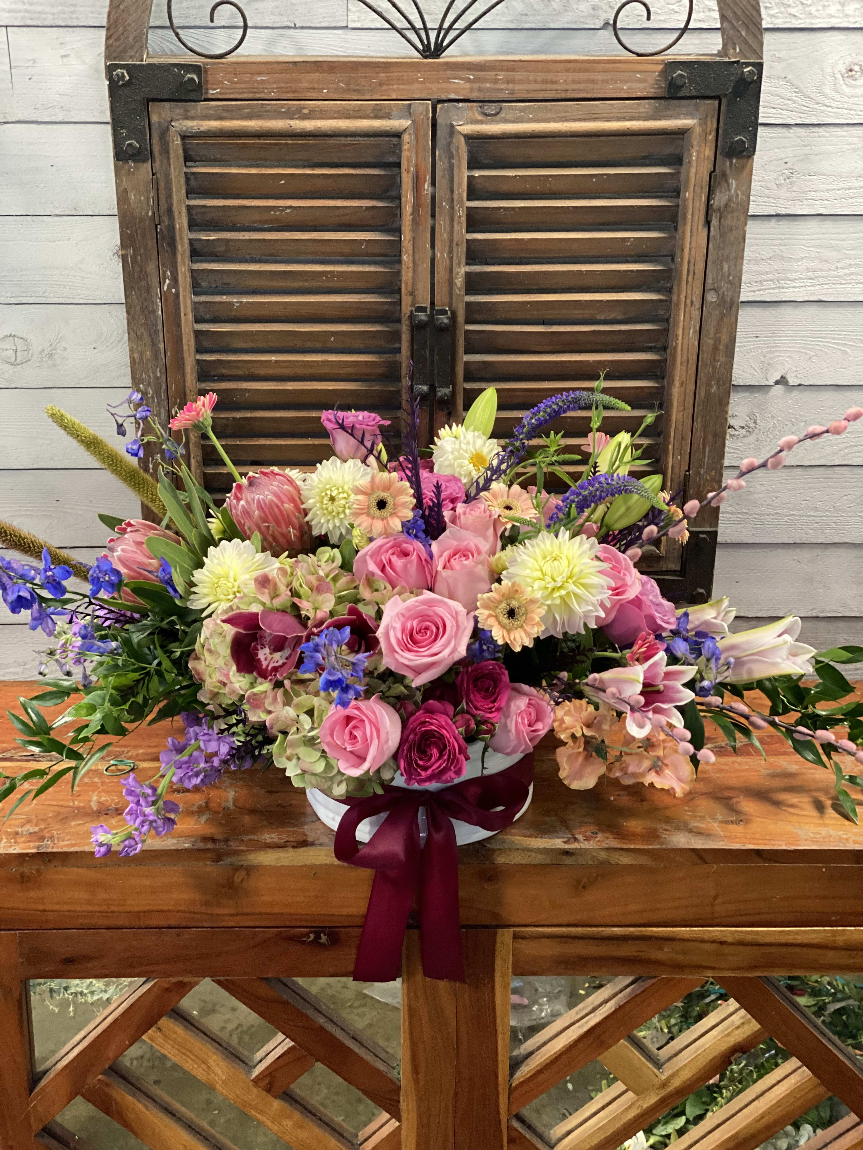 Mixed pink and purple flower arrangement in a white vase with ribbon
