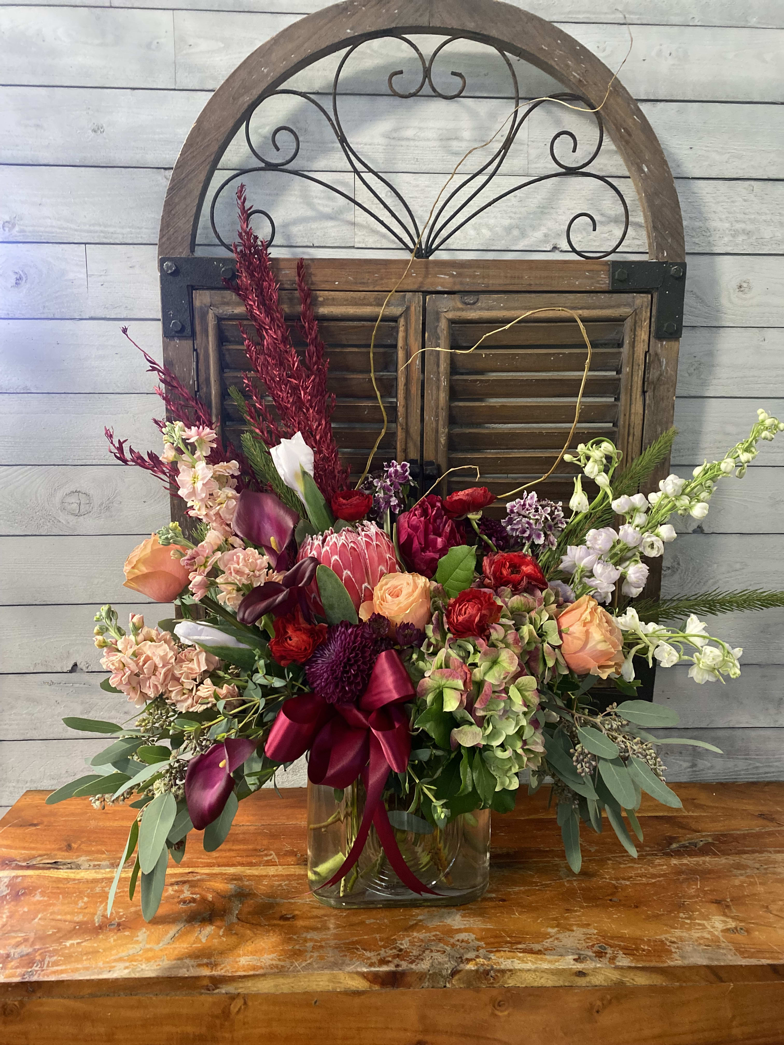 Mixed floral arrangement in a glass vase with burgundy ribbon