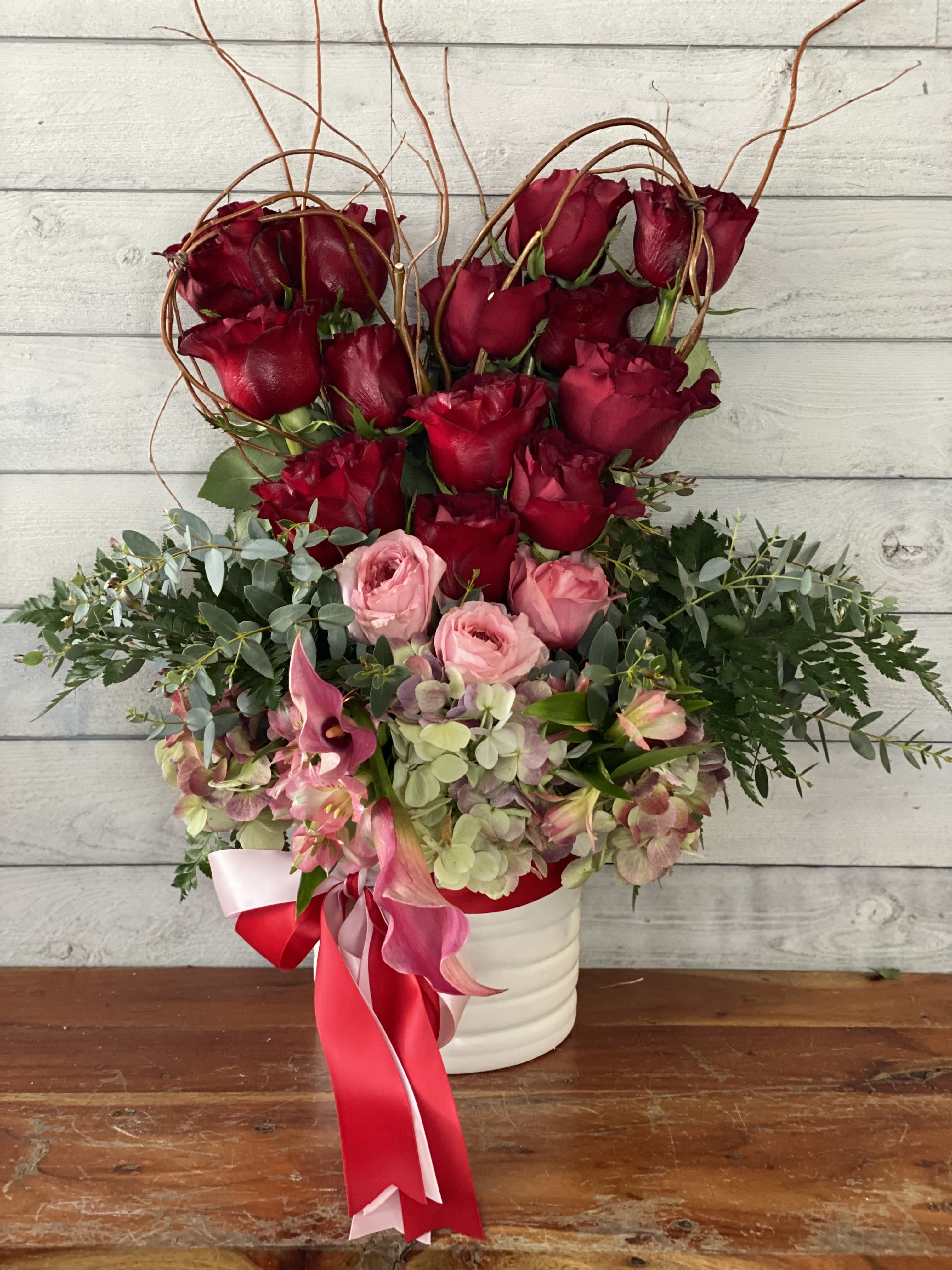 Red roses and pink flowers arranged in a white vase with ribbon