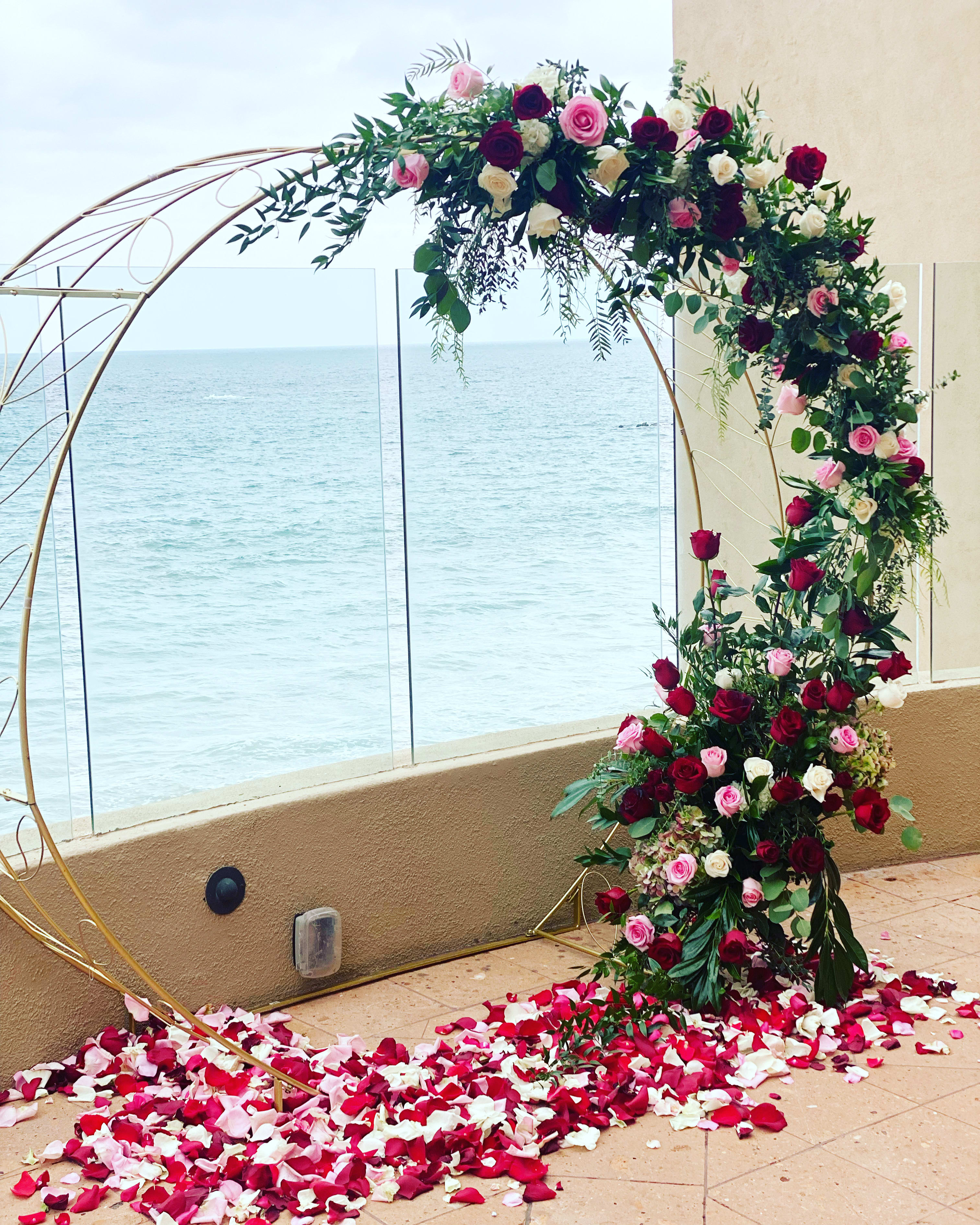 Floral arch with red, pink, and white roses over a petal-covered floor