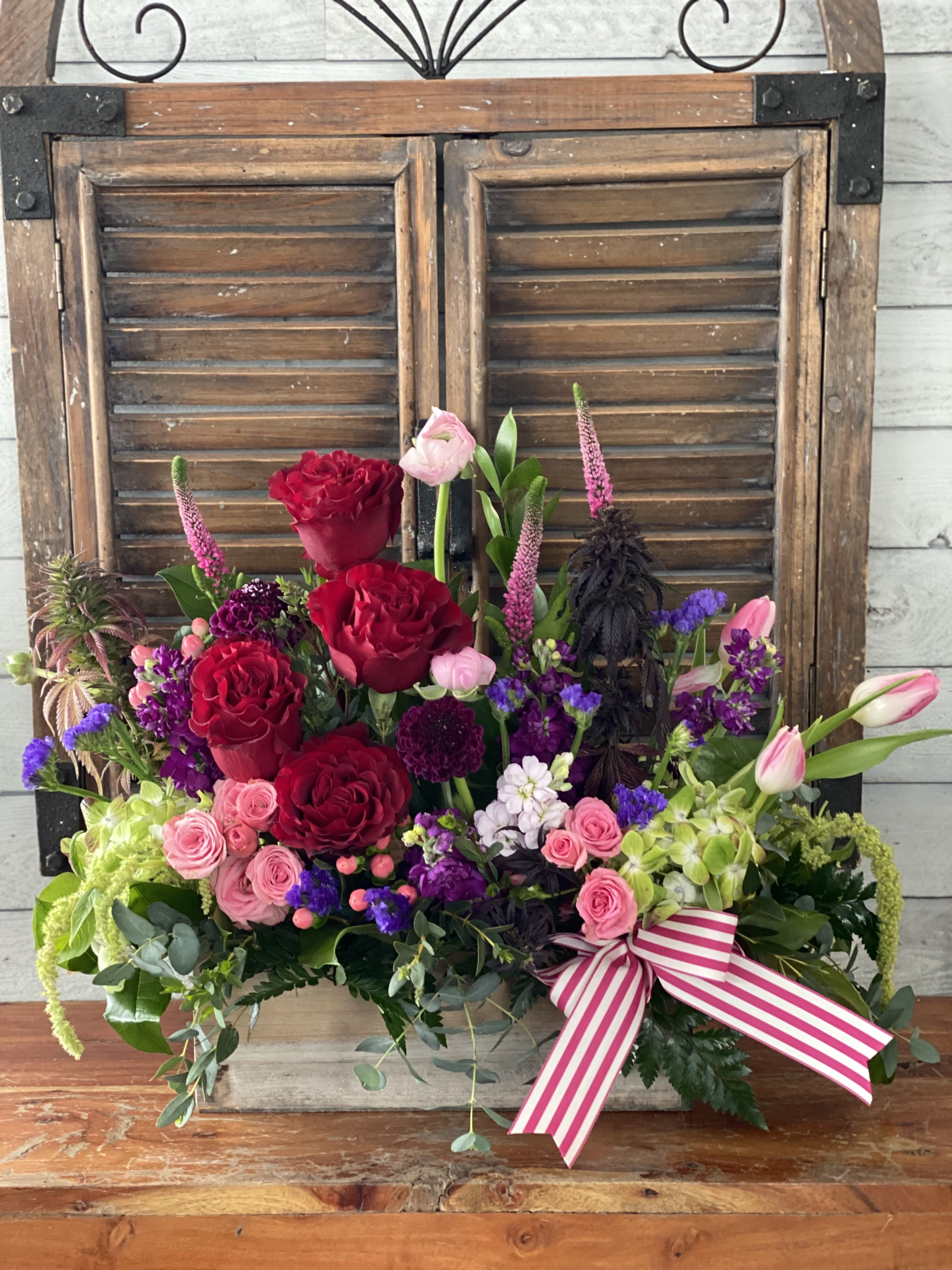 Mixed bouquet of red and pink roses with purple accents and a striped ribbon
