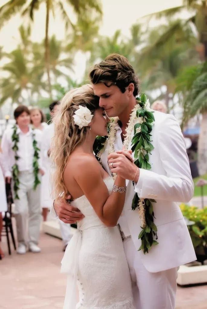 Bride and groom in white with floral leis and a white flower in her hair