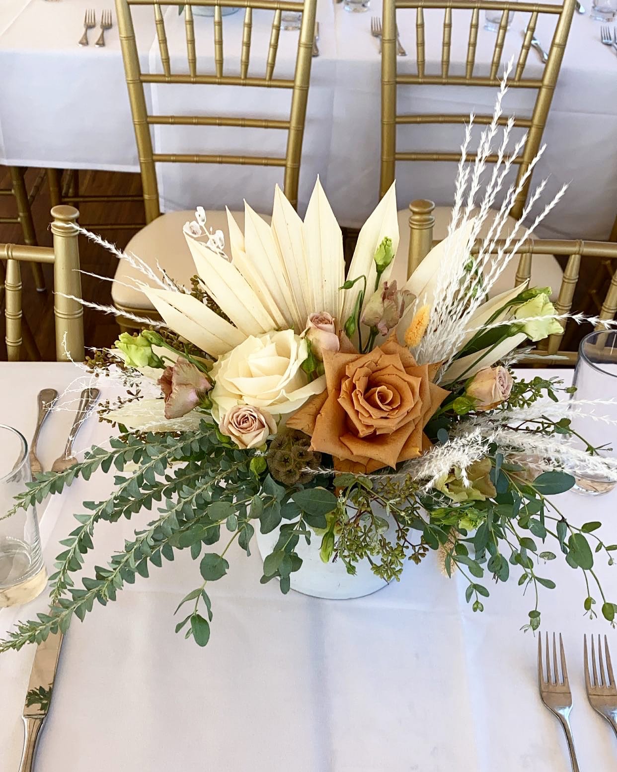 Low floral centerpiece with cream and tan roses on a white table