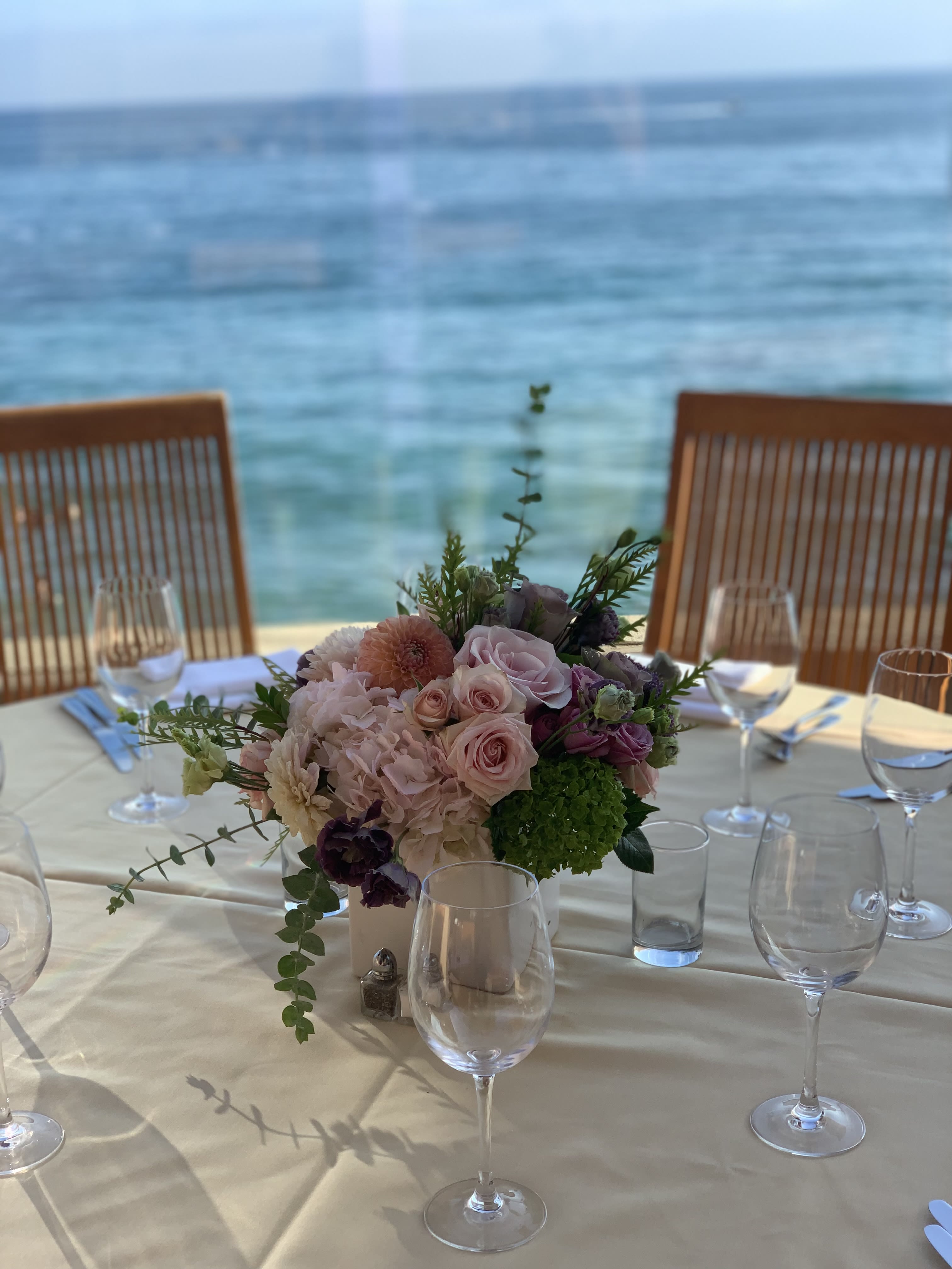 Pastel floral centerpiece in a white vase on a set dining table by the water
