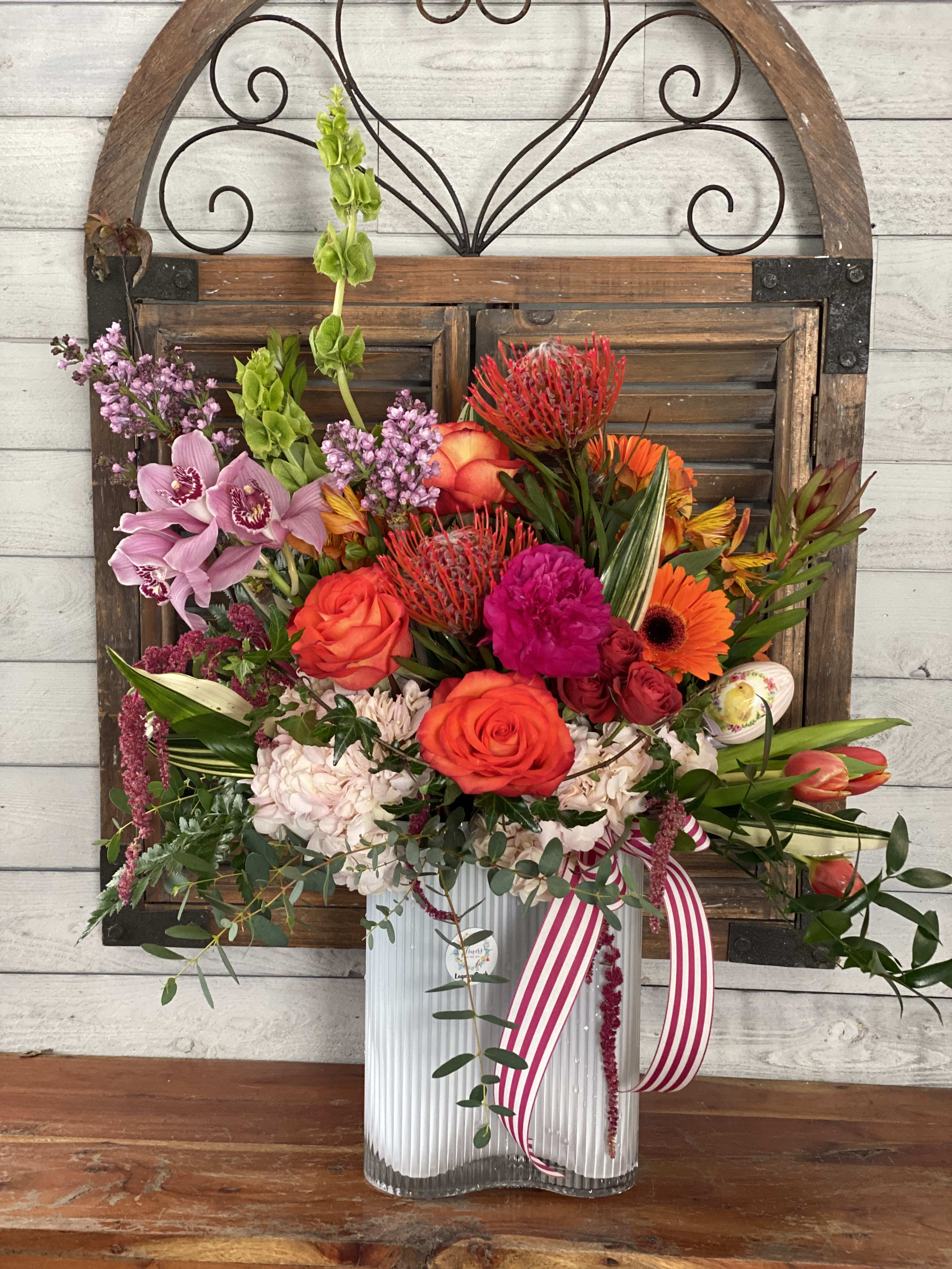 Colorful mixed flower arrangement in a clear ribbed vase with a striped ribbon
