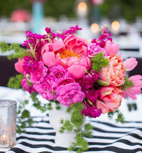 Pink and coral flowers arranged in a white vase on a striped tablecloth.