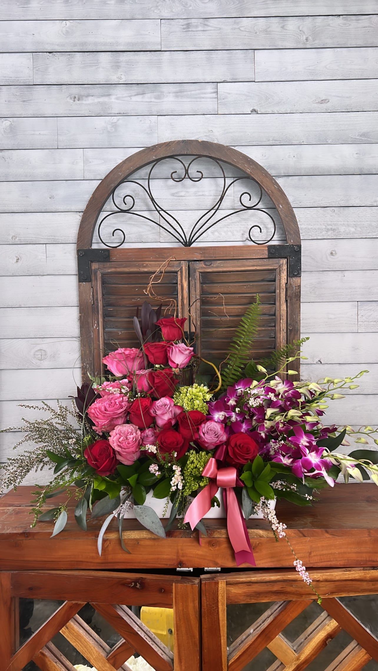 Mixed pink and red roses with purple orchids in a white container