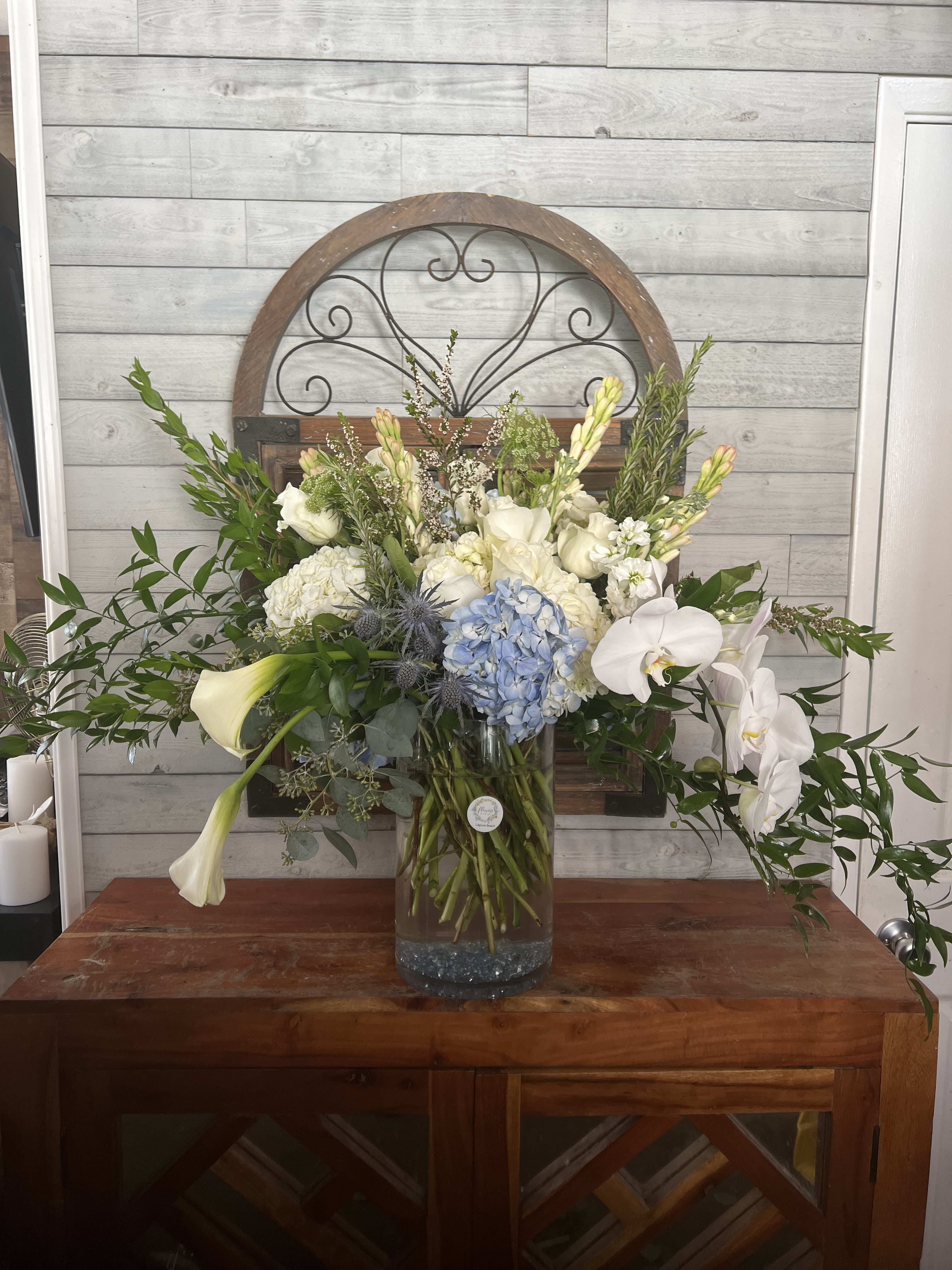 Large white and blue floral arrangement in a glass vase